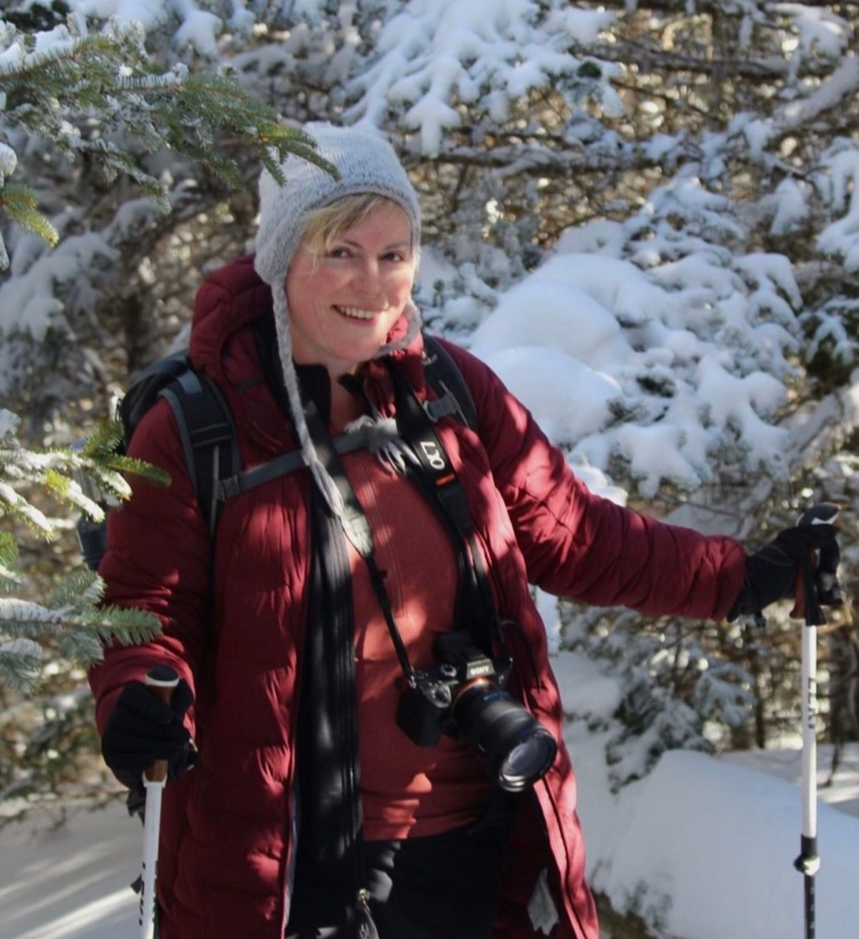 Female hiker in red puffer jacket smiling while hiking through a snow-covered pine forest on the Appalachian trail.