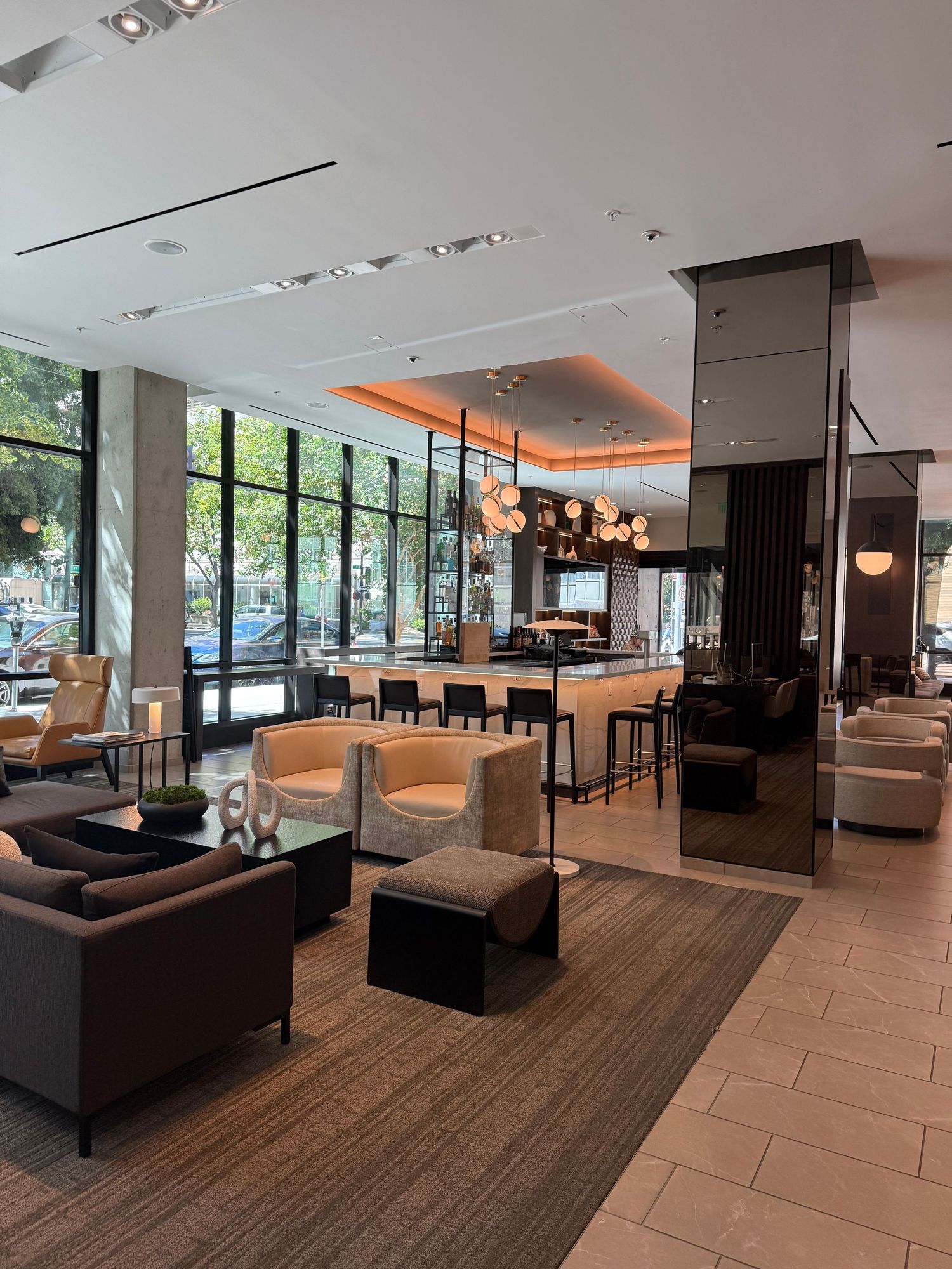 Modern hotel lobby with sleek lounge seating, a bar area, floor-to-ceiling windows, and warm ambient lighting.