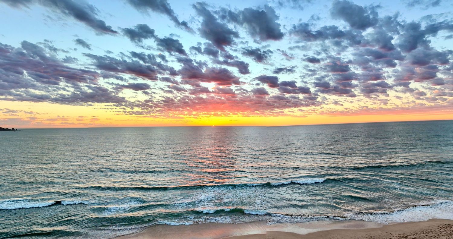Stunning colorful sunset over calm ocean waves with vibrant pink and purple clouds on the horizon.