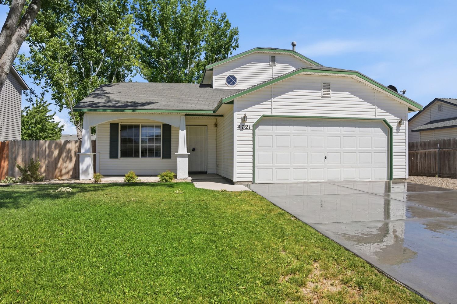 Single-story suburban home with white siding, two-car garage, manicured lawn, and mature shade trees.