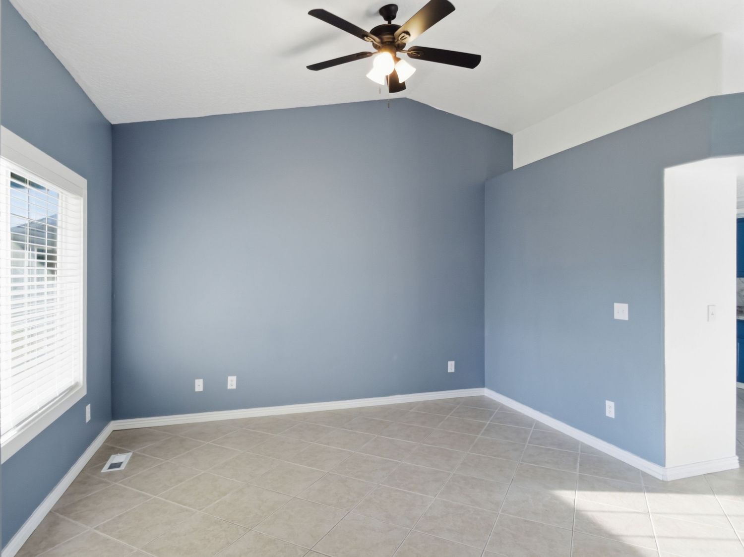 Empty bedroom with blue-gray walls, vaulted ceiling, ceiling fan, and tile flooring awaiting furnishing.