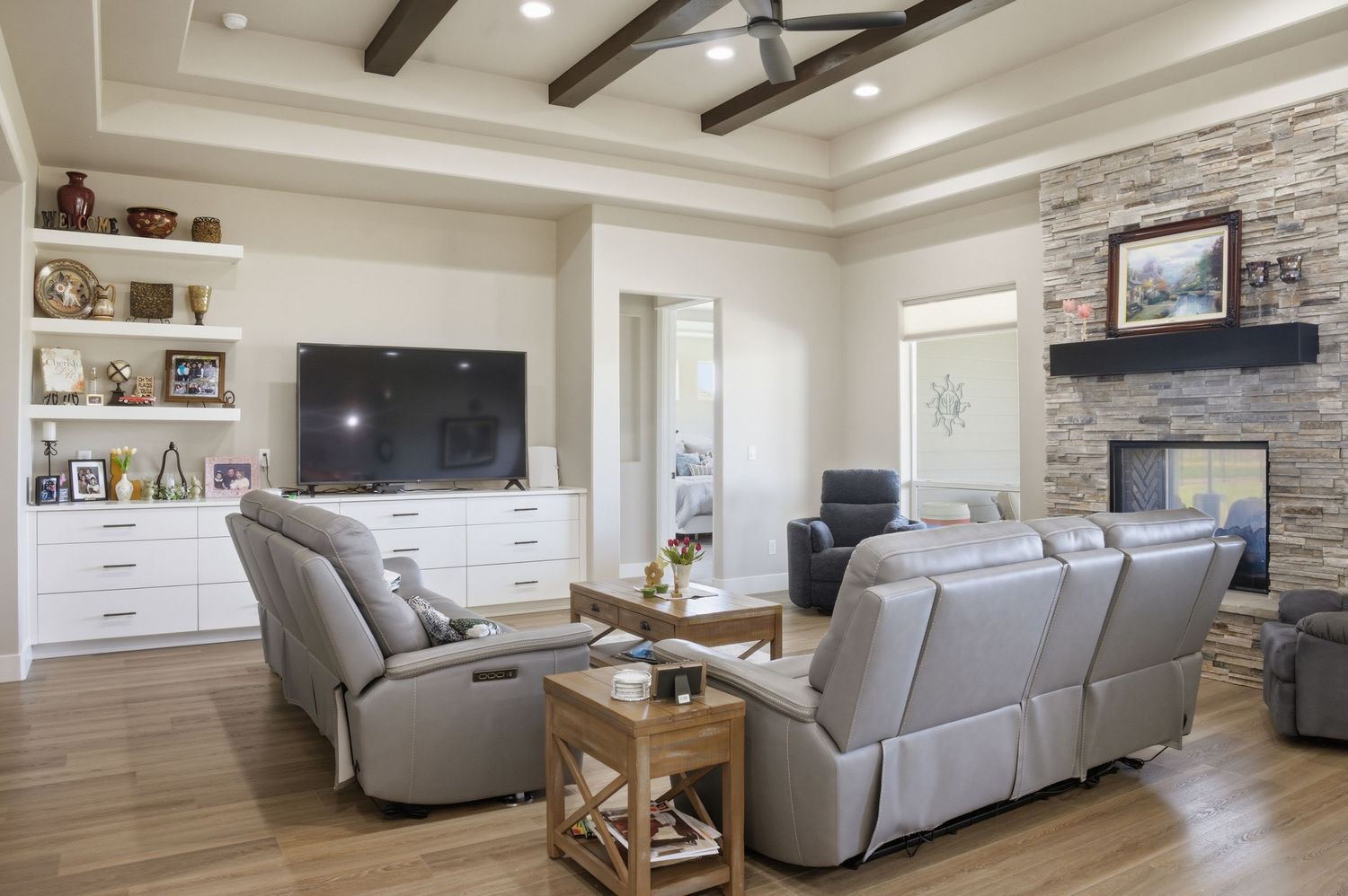 Spacious living room with gray leather recliners, stone fireplace, built-in shelves, and wood beam ceiling.
