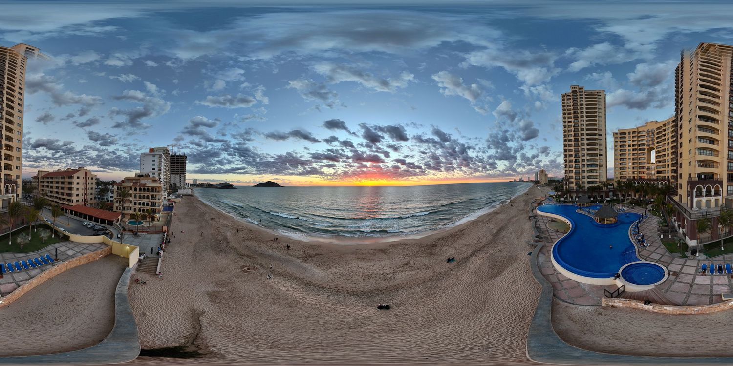 Panoramic beachfront sunset view with high-rise hotels, pool, and dramatic cloudy sky in a coastal city.