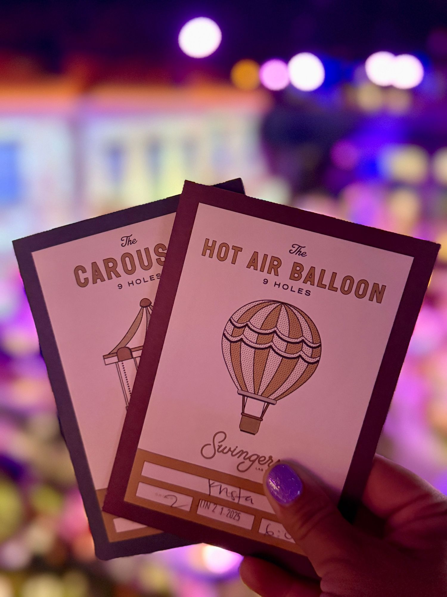 Two mini golf scorecards for The Carousel and Hot Air Balloon courses held up at Swingers venue.