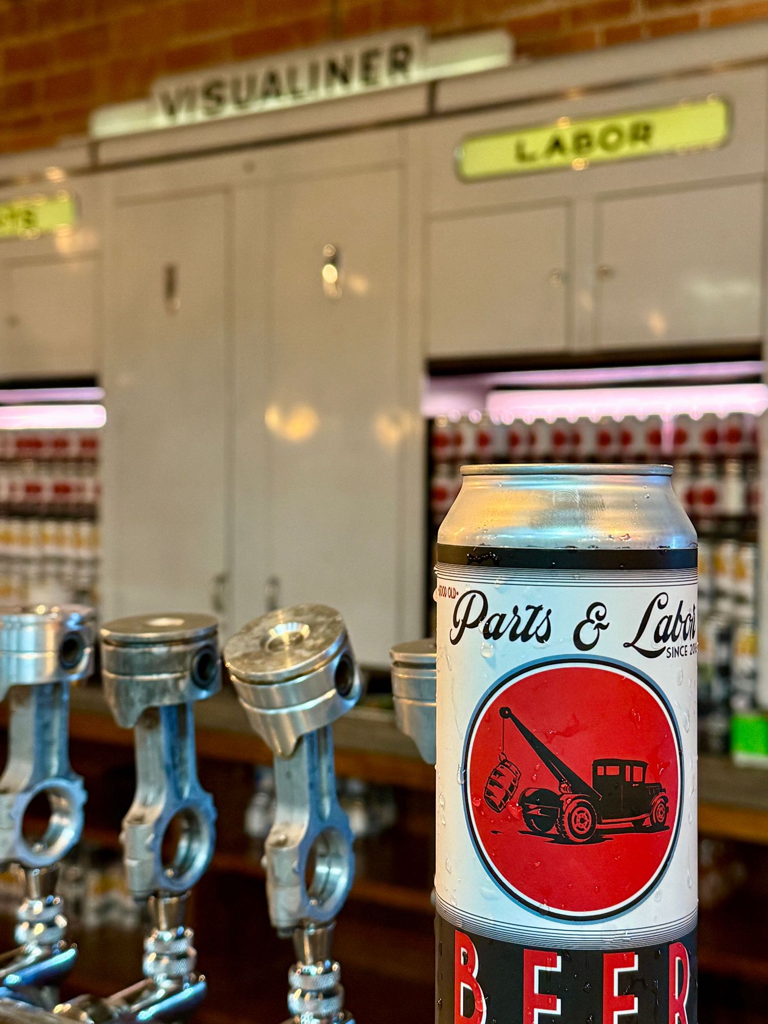 Parts & Labor Brewing Co. beer can displayed on a bar with piston tap handles and vintage decor.
