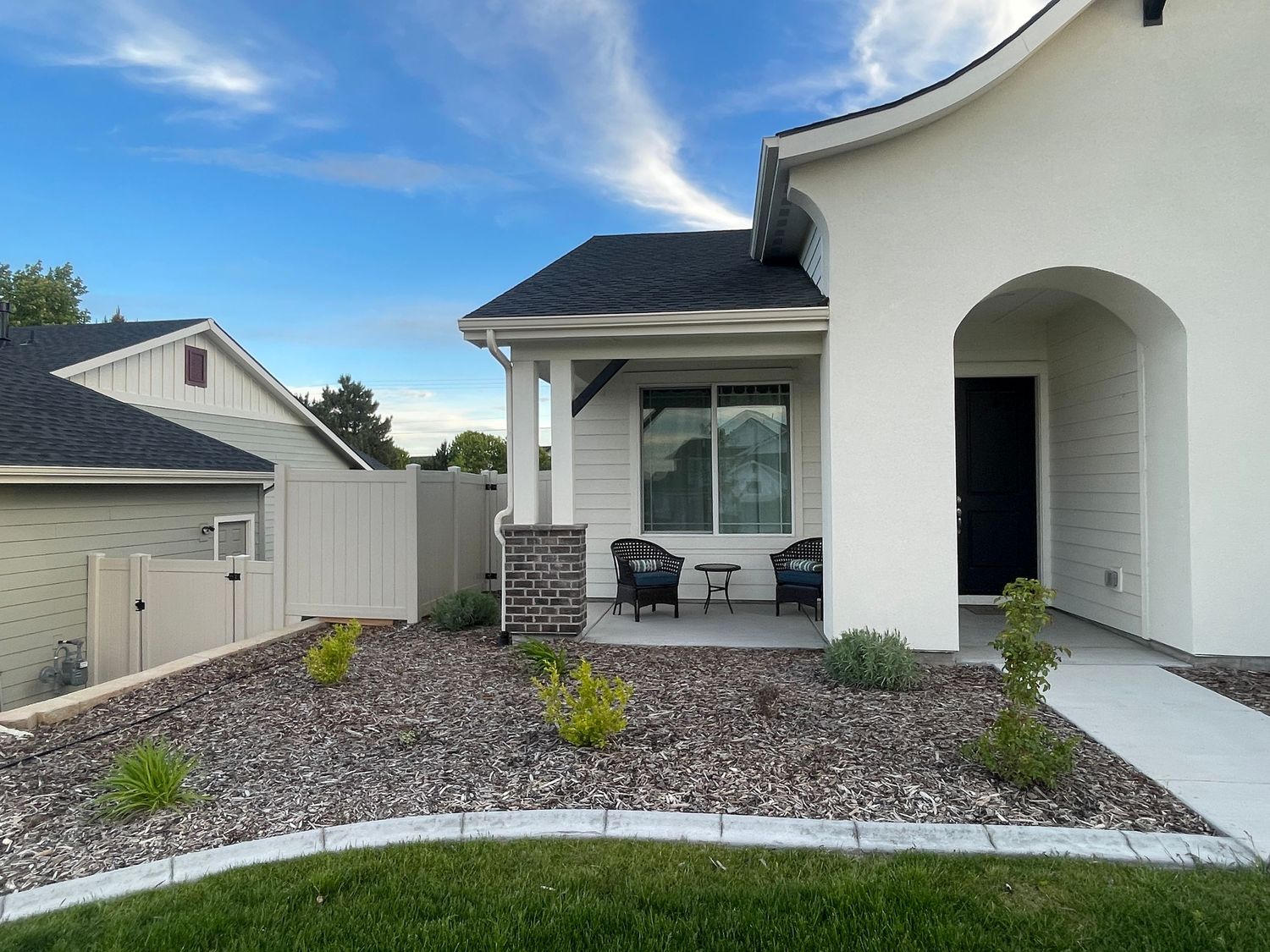 Modern white home exterior featuring arched entryway, rock landscaping, patio seating, and decorative fence.
