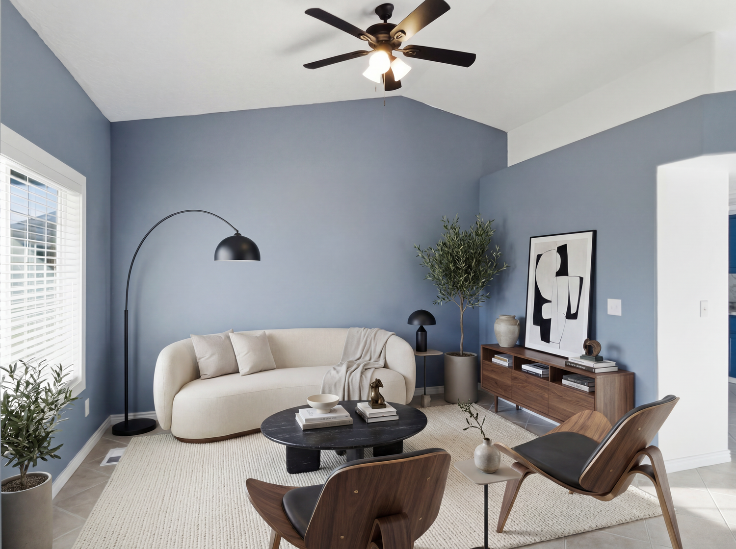 Modern living room with blue-gray walls, curved cream sofa, wooden furniture, and vaulted ceiling fan.