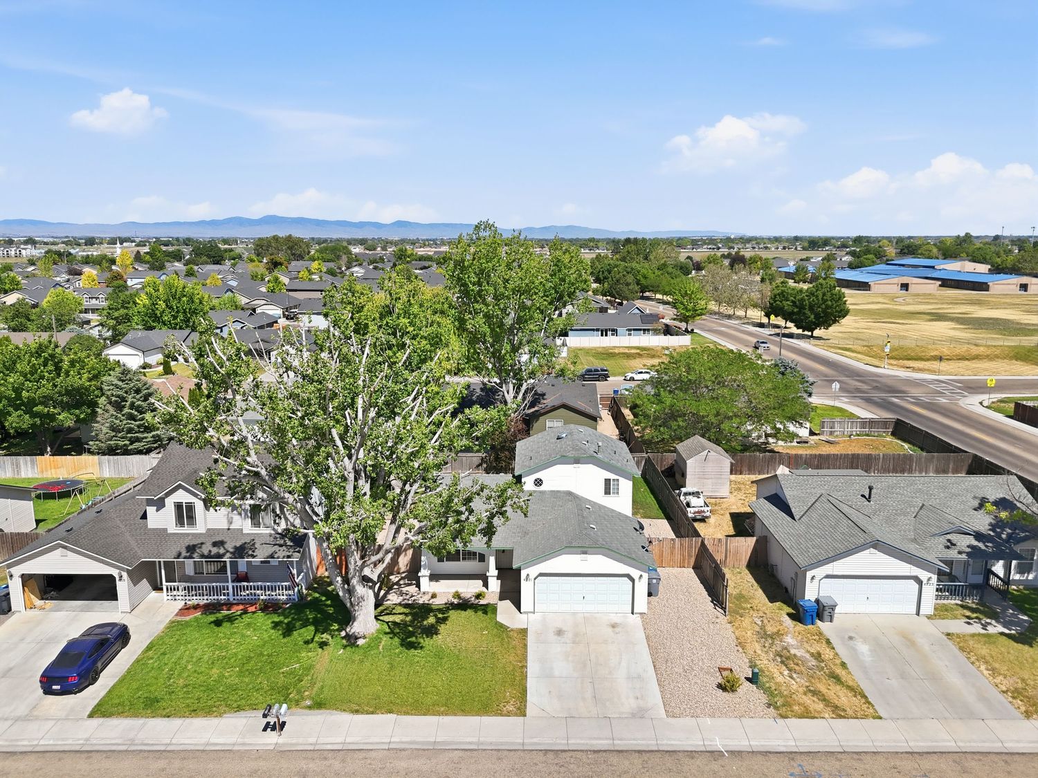Aerial view of a suburban neighborhood with green lawns, homes, and mountain views in the distance.