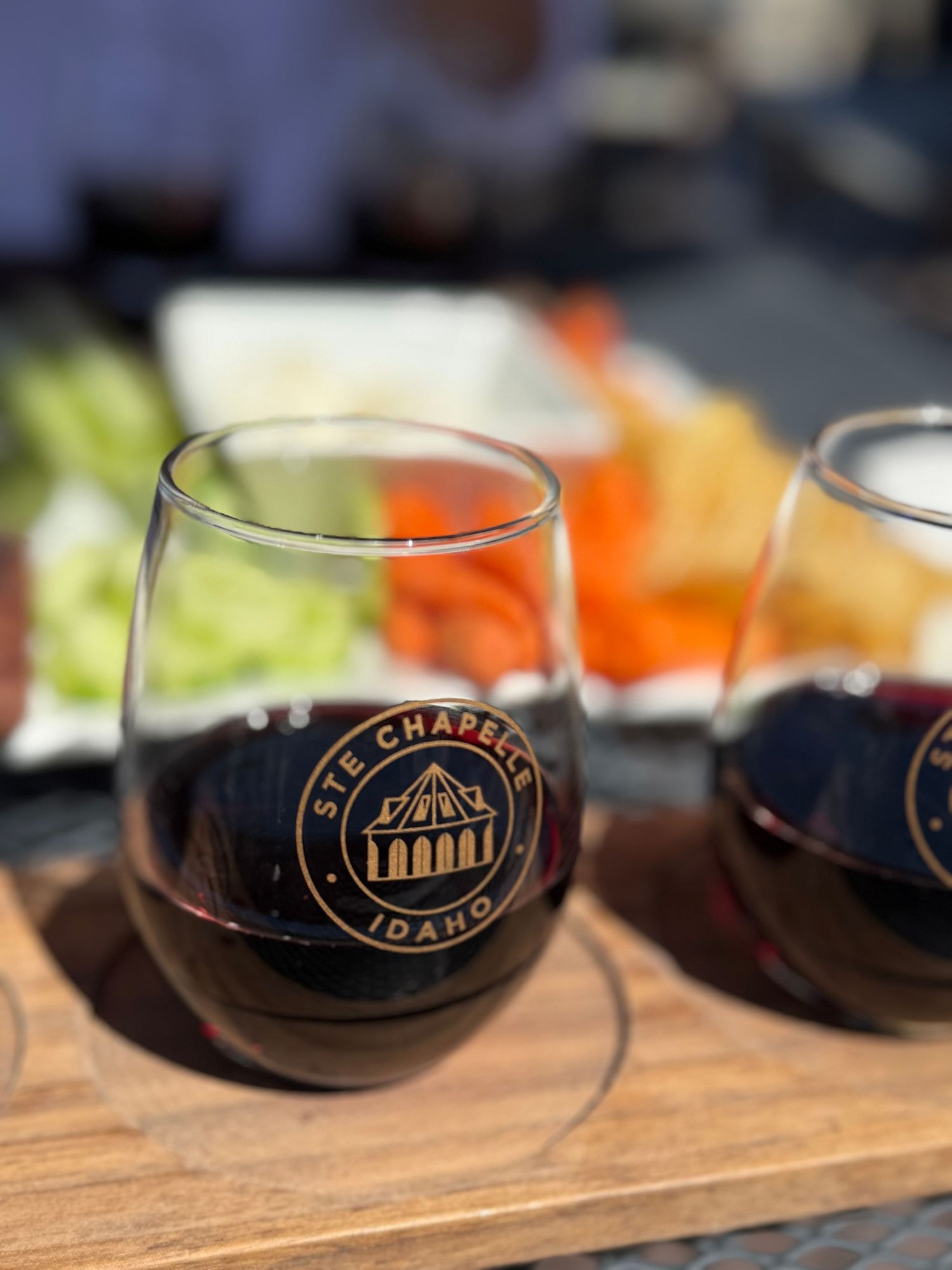 Two Ste. Chapelle Idaho branded stemless wine glasses filled with red wine on a wooden tray.