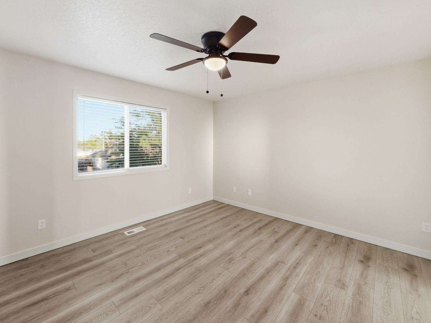 Empty bedroom with light wood floors, white walls, and a ceiling fan with dark blades.