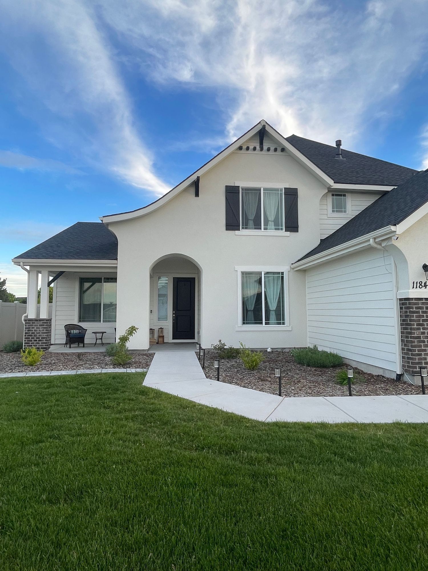 White two-story craftsman home with black shutters, arched entry, attached garage, and lush green lawn.