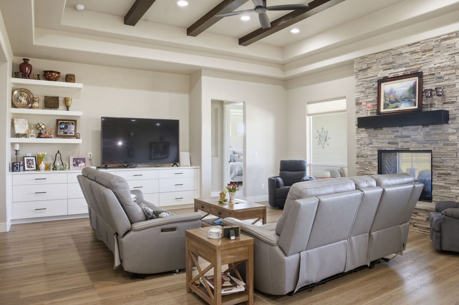 Spacious living room with gray recliners, stone fireplace, wood beam ceiling, and built-in white shelving.
