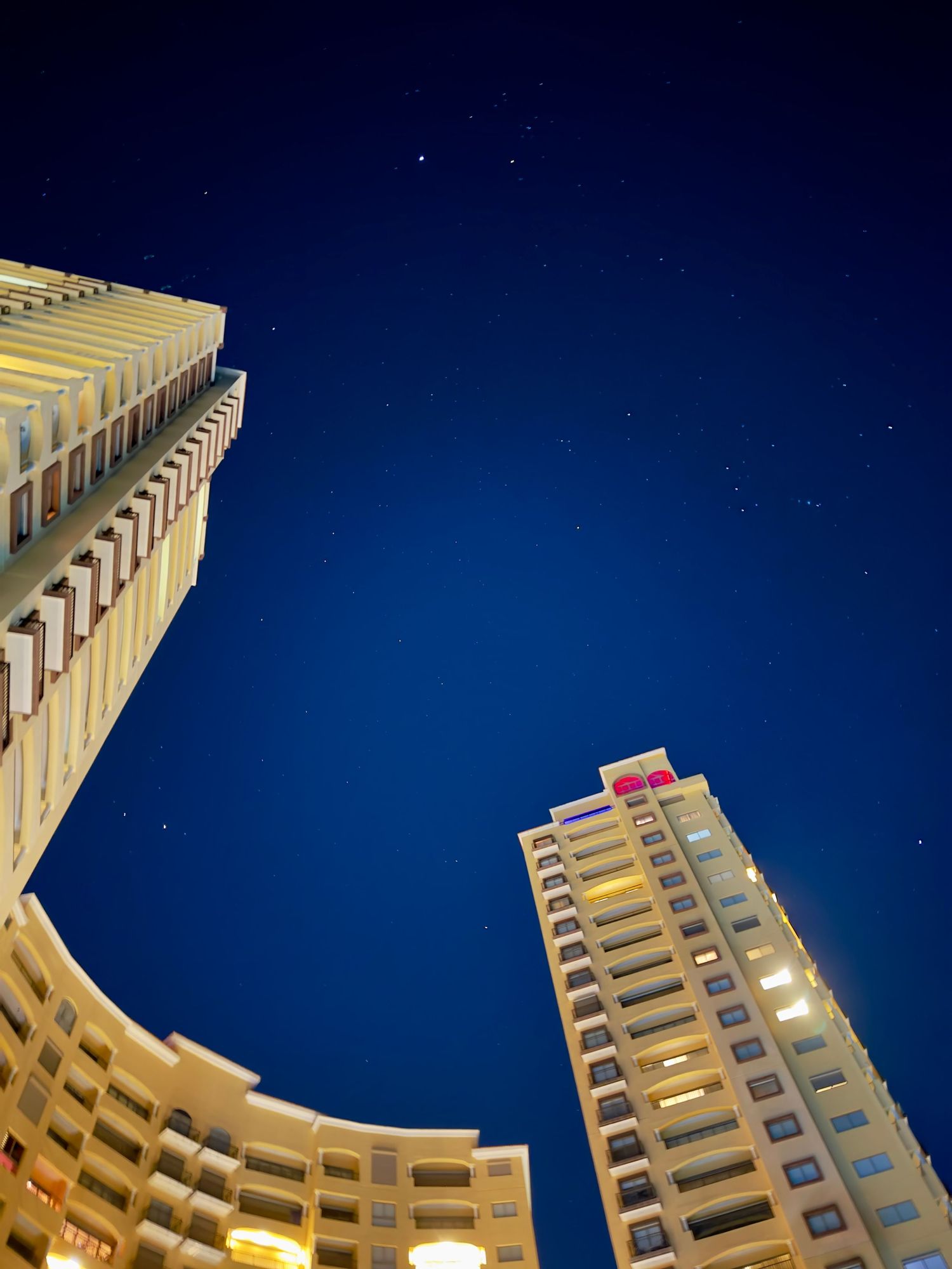 Low-angle night view of two illuminated high-rise hotel towers against a deep blue starry sky.