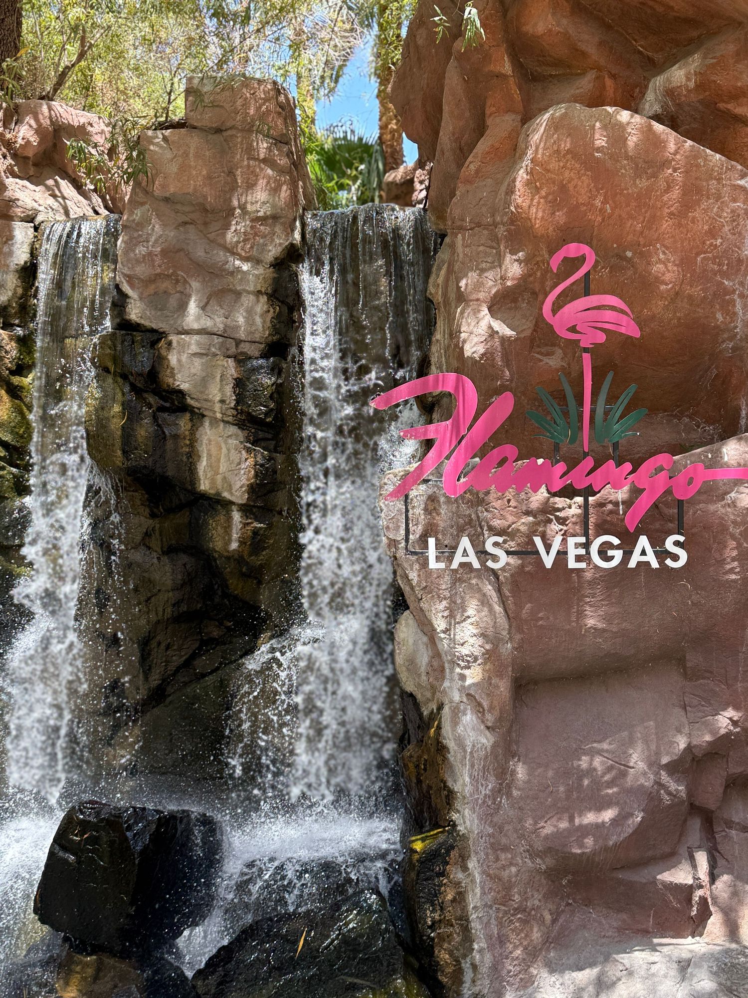 Flamingo Las Vegas hotel sign beside a rocky waterfall feature at the iconic Strip casino resort.