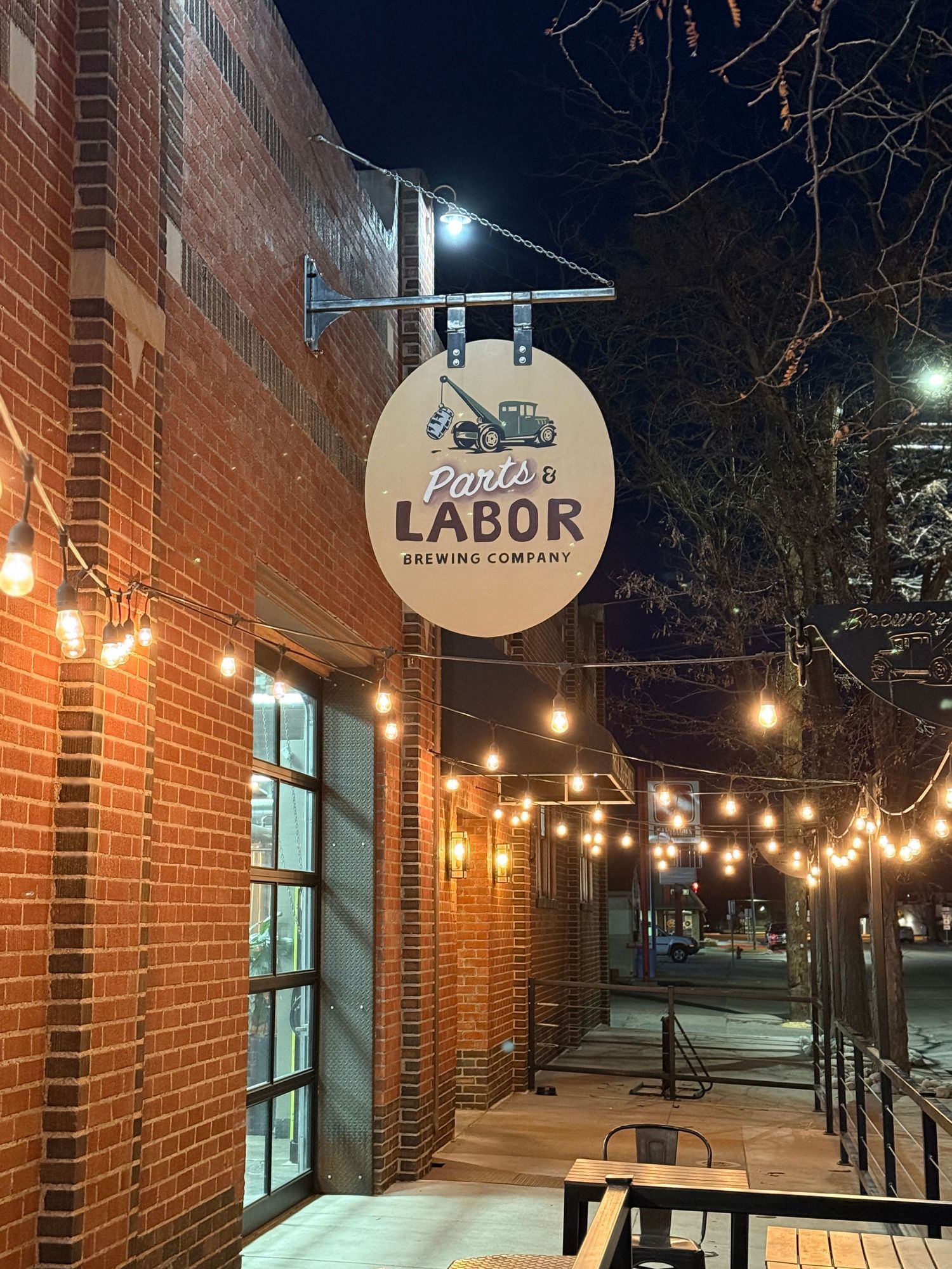 Parts & Labor Brewing Company sign on a brick building exterior with string lights at night.