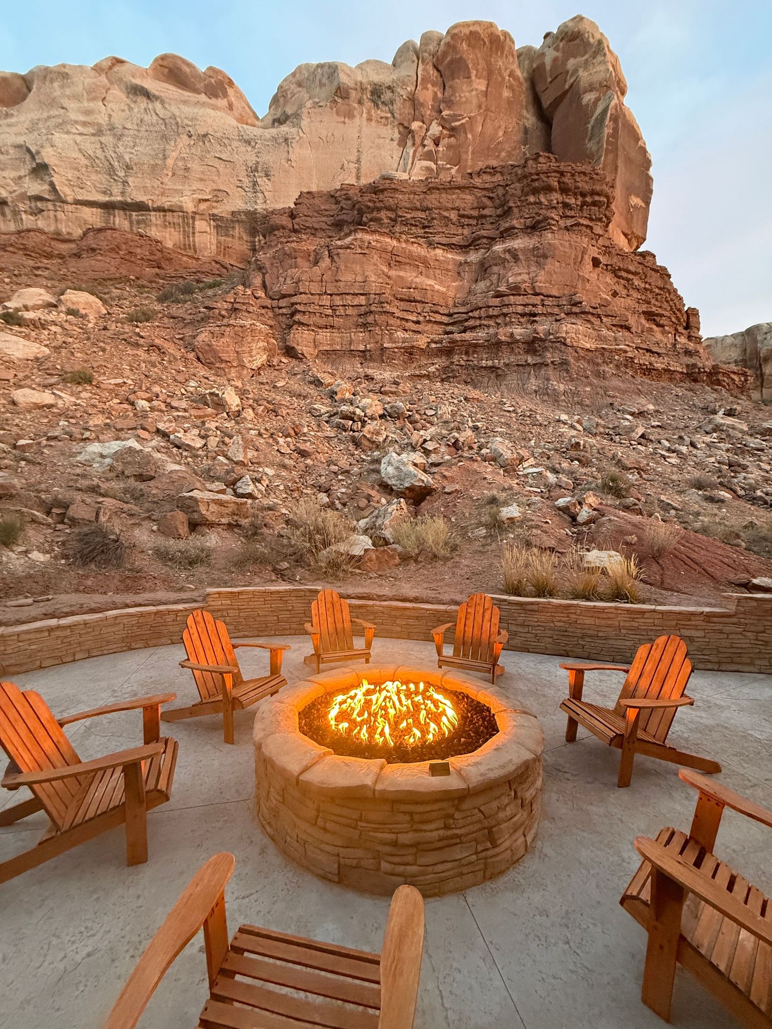 Circular fire pit surrounded by wooden Adirondack chairs on patio with dramatic red rock canyon backdrop.