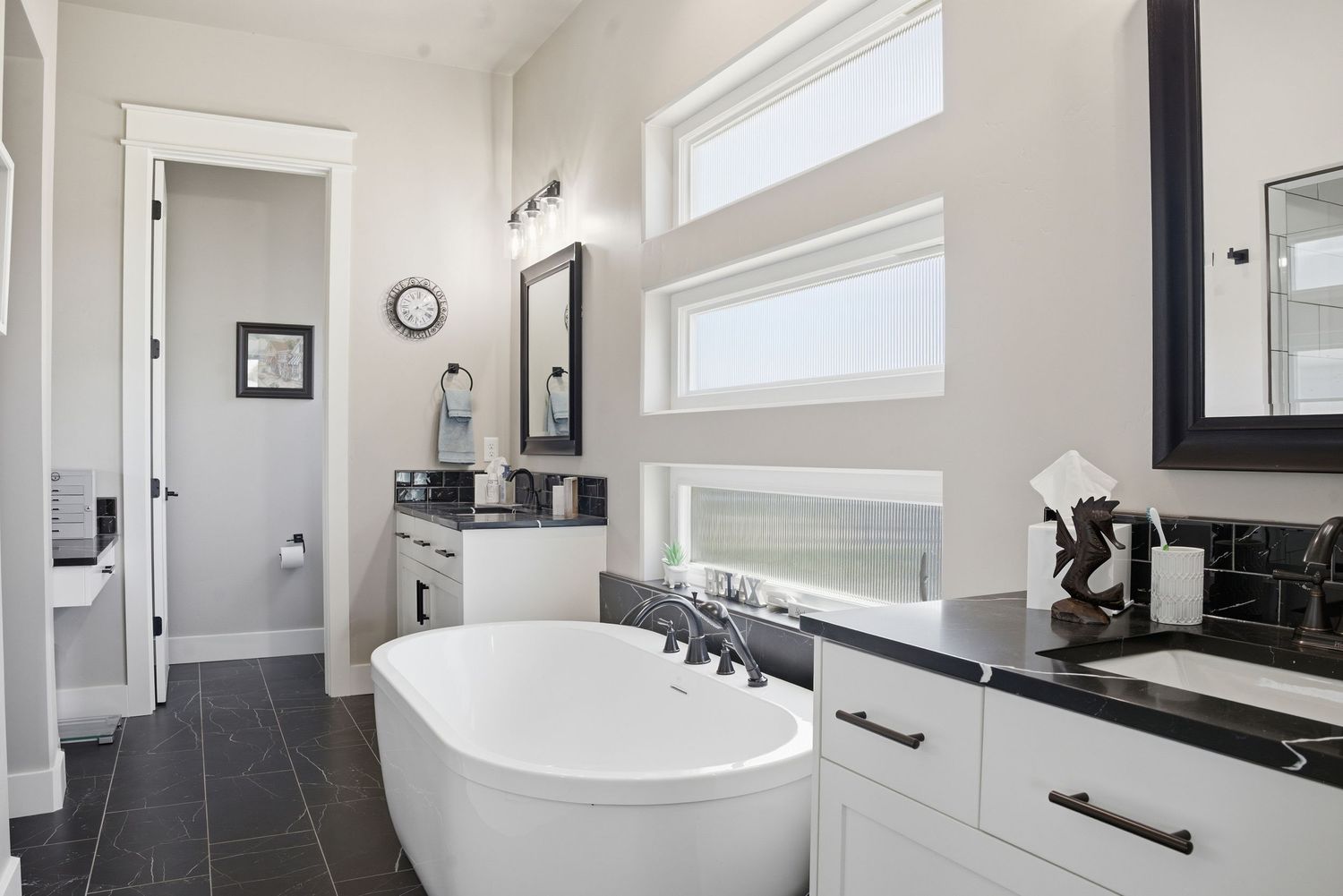 Elegant master bathroom with freestanding soaking tub, dual vanities, black fixtures, and large windows.