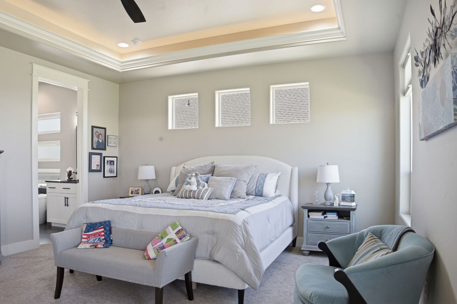 Bright master bedroom with tray ceiling, upholstered headboard, neutral decor, and en-suite bathroom access.