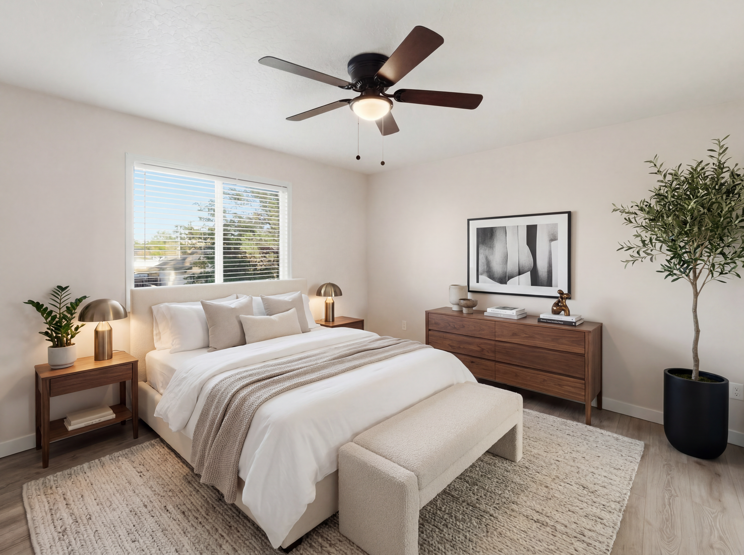 Bright bedroom with a large bed, wood dresser, ceiling fan, and potted tree near the window.