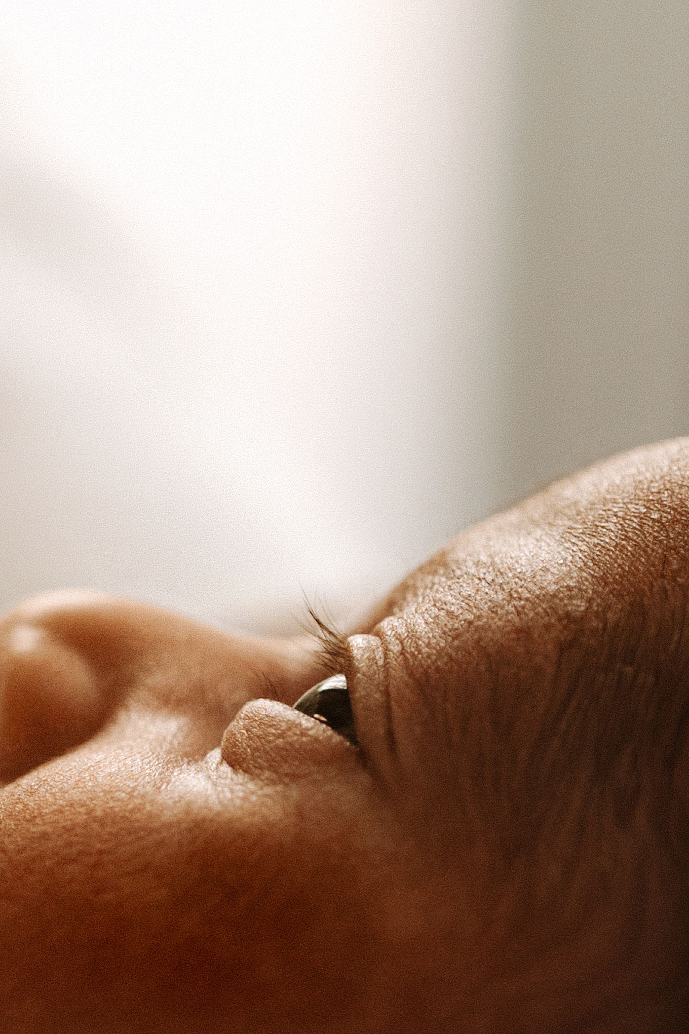 Close-up macro photo of a newborn baby's eye and eyelashes with soft warm skin tones.