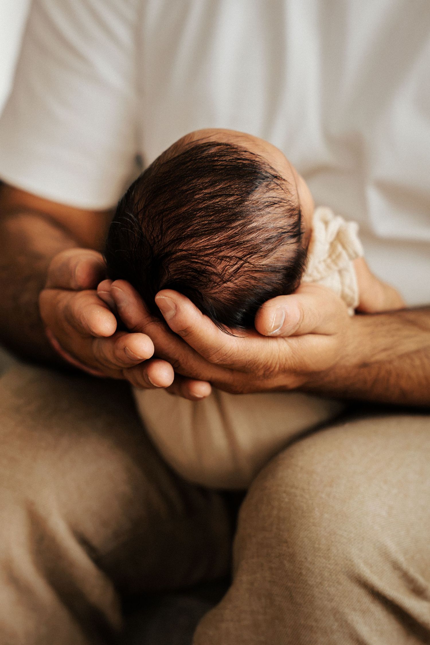 An adult cradling a newborn baby's head gently in both hands, close-up shot of tender parental moment.