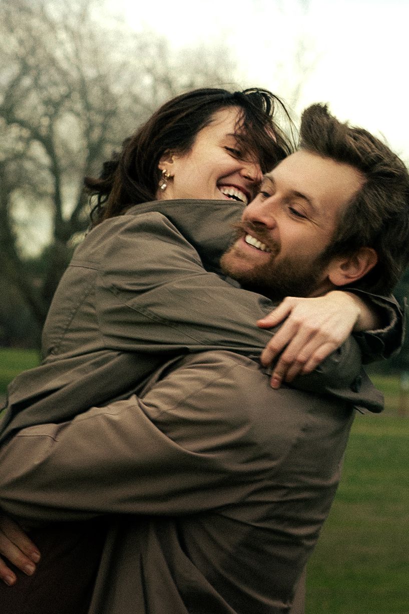 Happy couple hugging and laughing joyfully in a park with bare trees in the background.