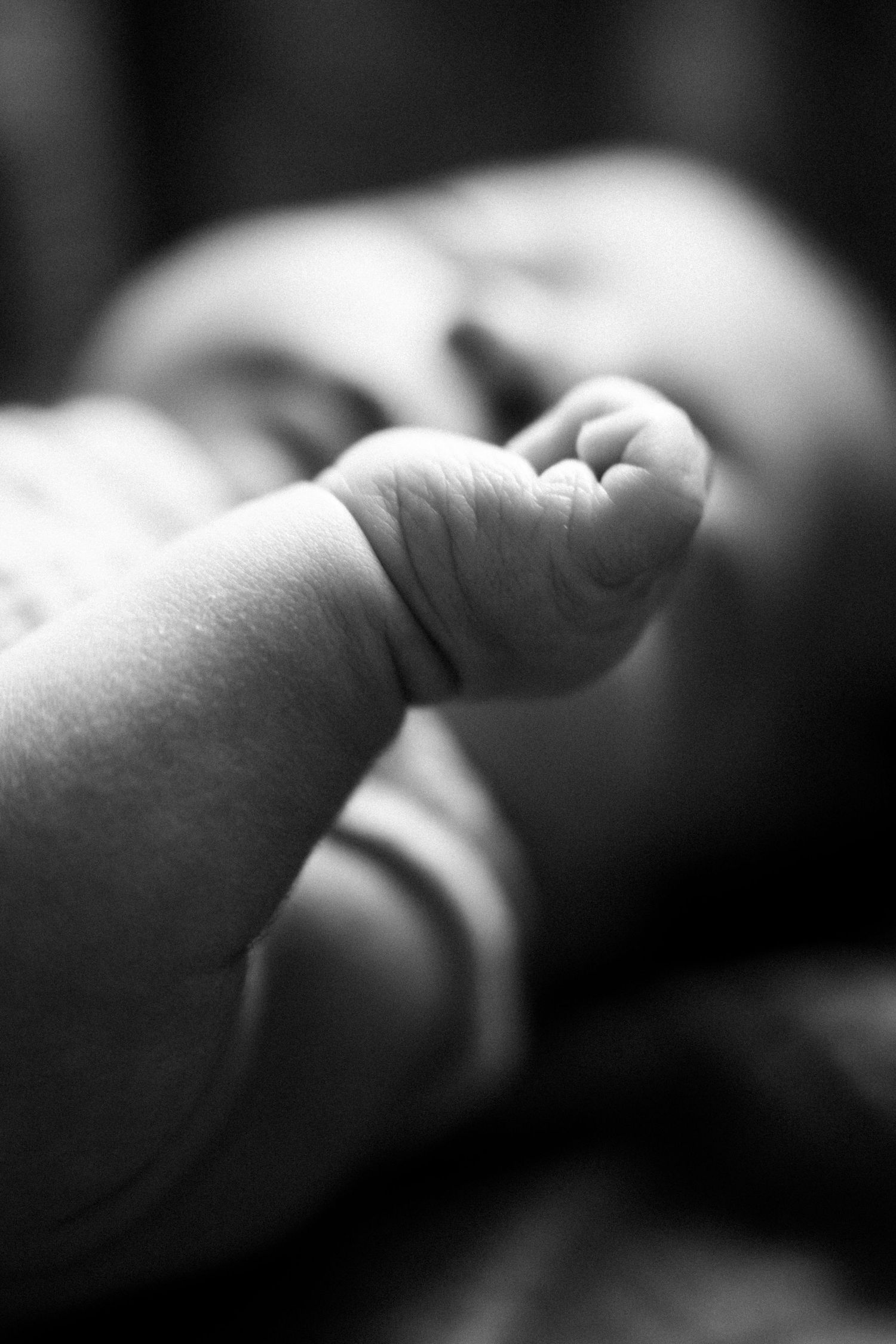 Close-up black and white photo of a newborn baby's tiny hand and feet, showcasing delicate wrinkled skin.