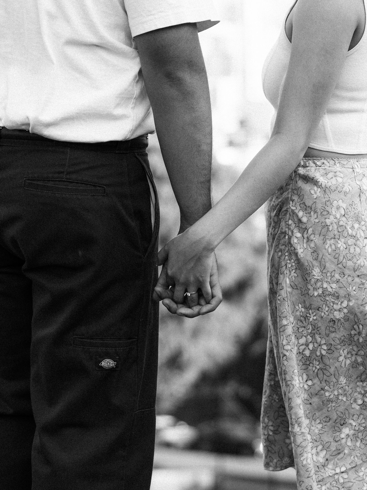 Black and white photo of a couple holding hands, woman wearing a floral skirt and ring, man in dark Dickies pants.
