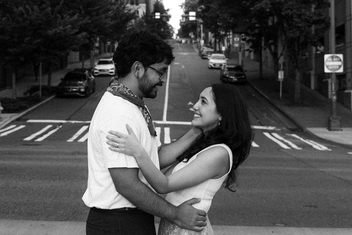 Black and white photo of a couple embracing and smiling at each other on a city street.