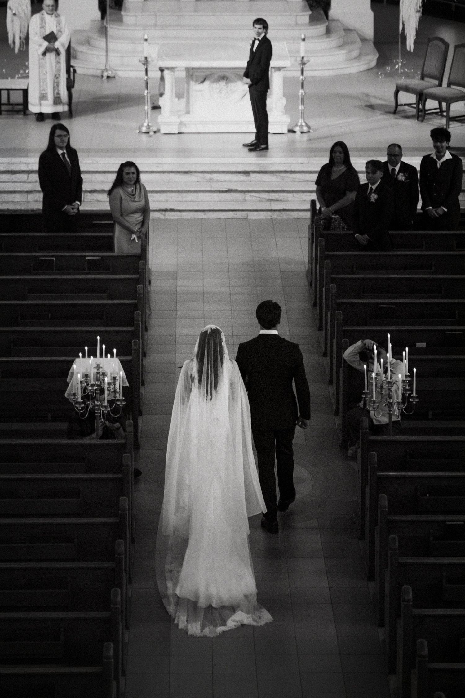 Black and white photo of a bride walking down the church aisle with escort toward the altar during a wedding ceremony.