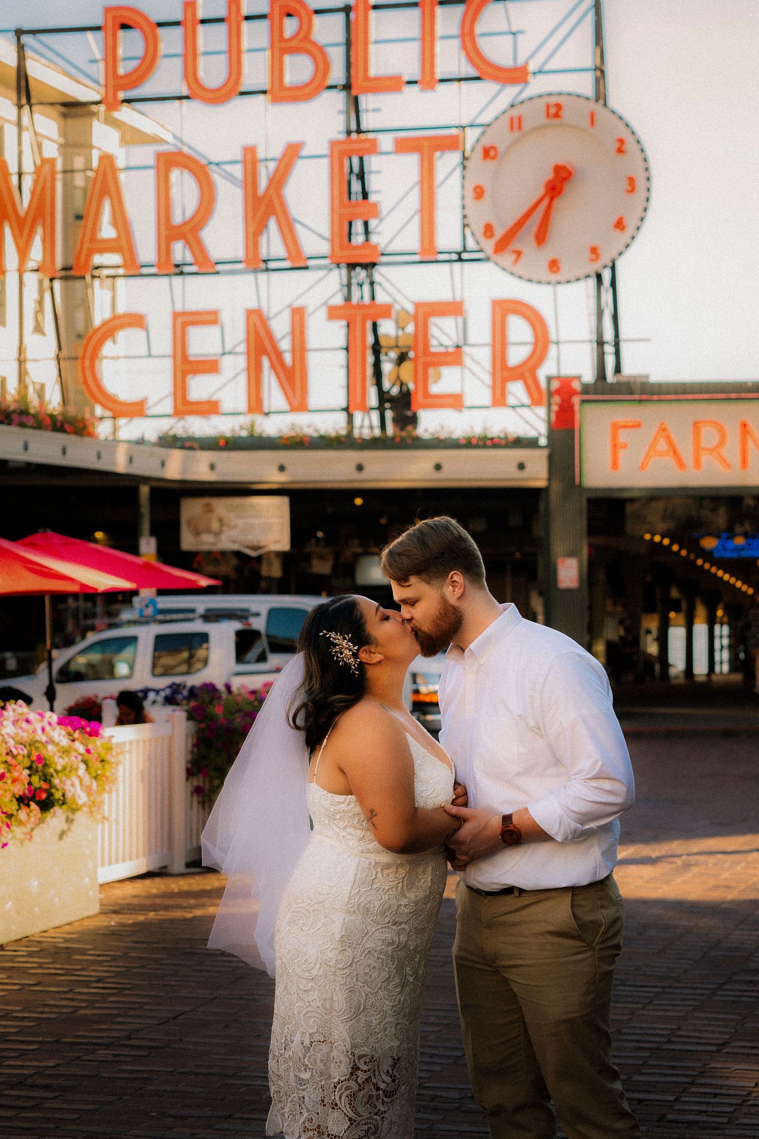 Couple sharing a kiss in wedding attire in front of the iconic Pike Place Market sign in Seattle, WA.