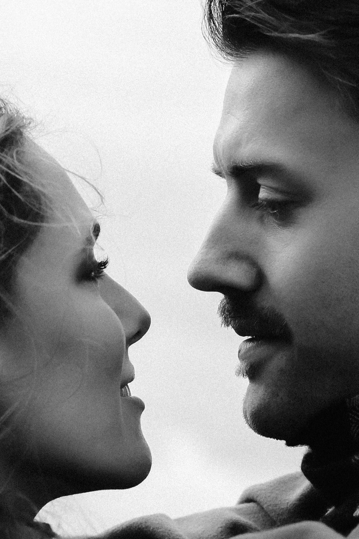 Black and white close-up portrait of a romantic couple facing each other, man with beard and woman with curly hair.