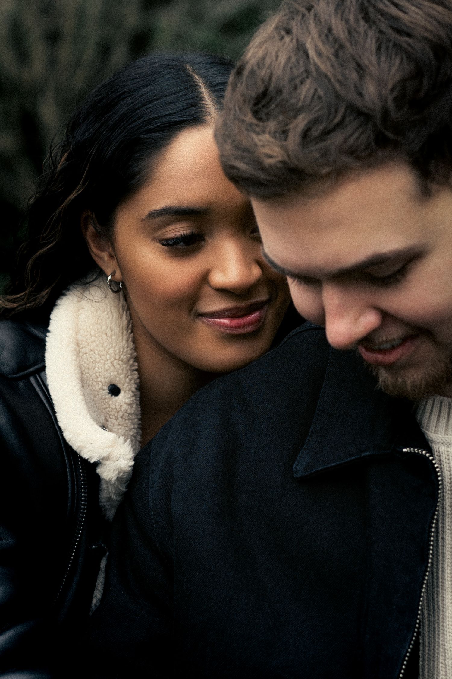 Interracial couple sharing a tender intimate moment outdoors, woman in black leather shearling jacket.