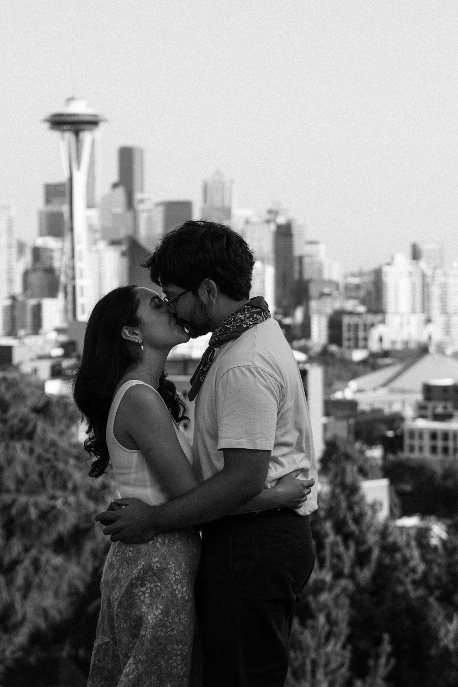 Couple sharing a romantic kiss with the Seattle skyline and Space Needle in the background, black and white photo.