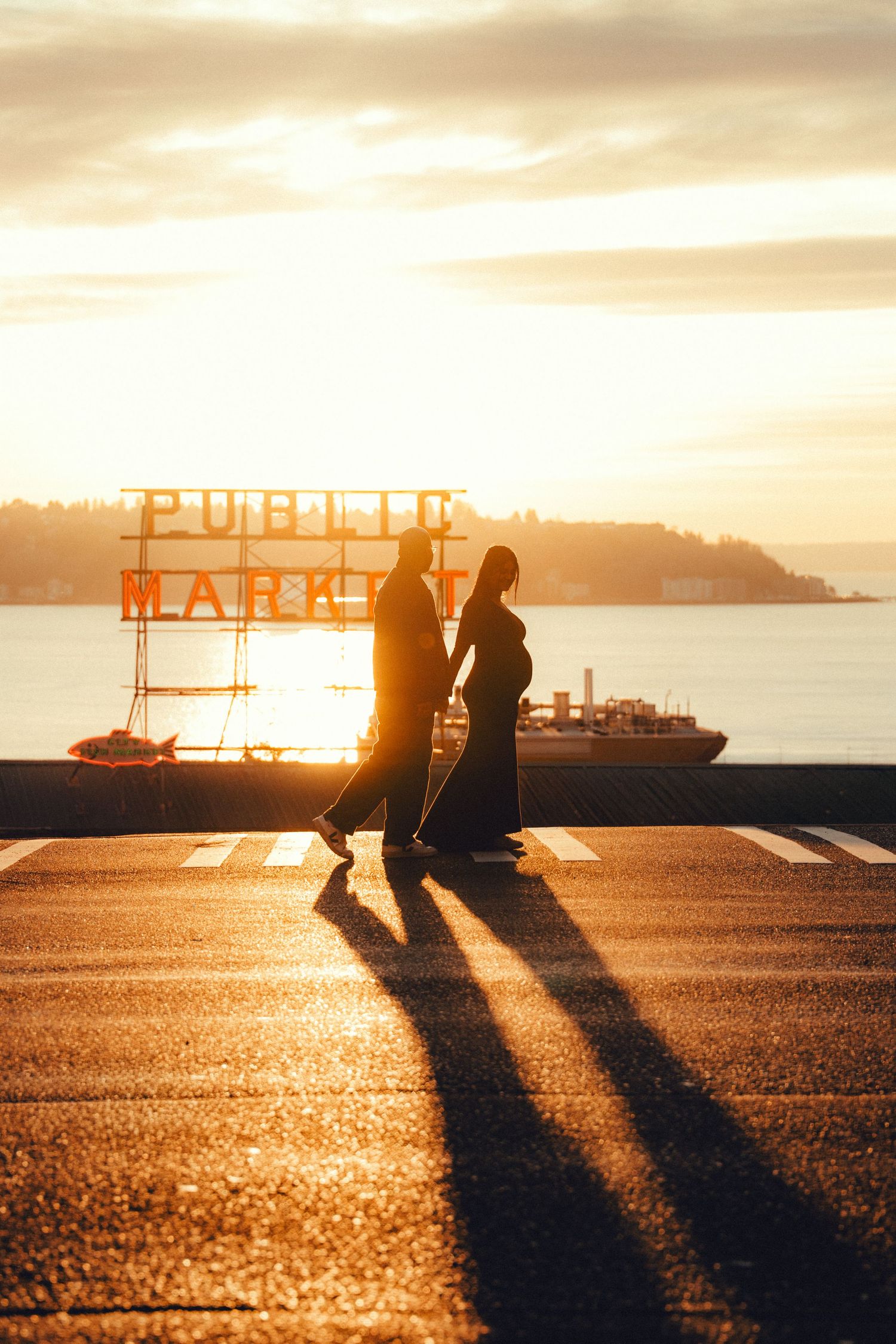 Silhouette of a pregnant couple walking at sunset near Pike Place Public Market sign in Seattle, WA.