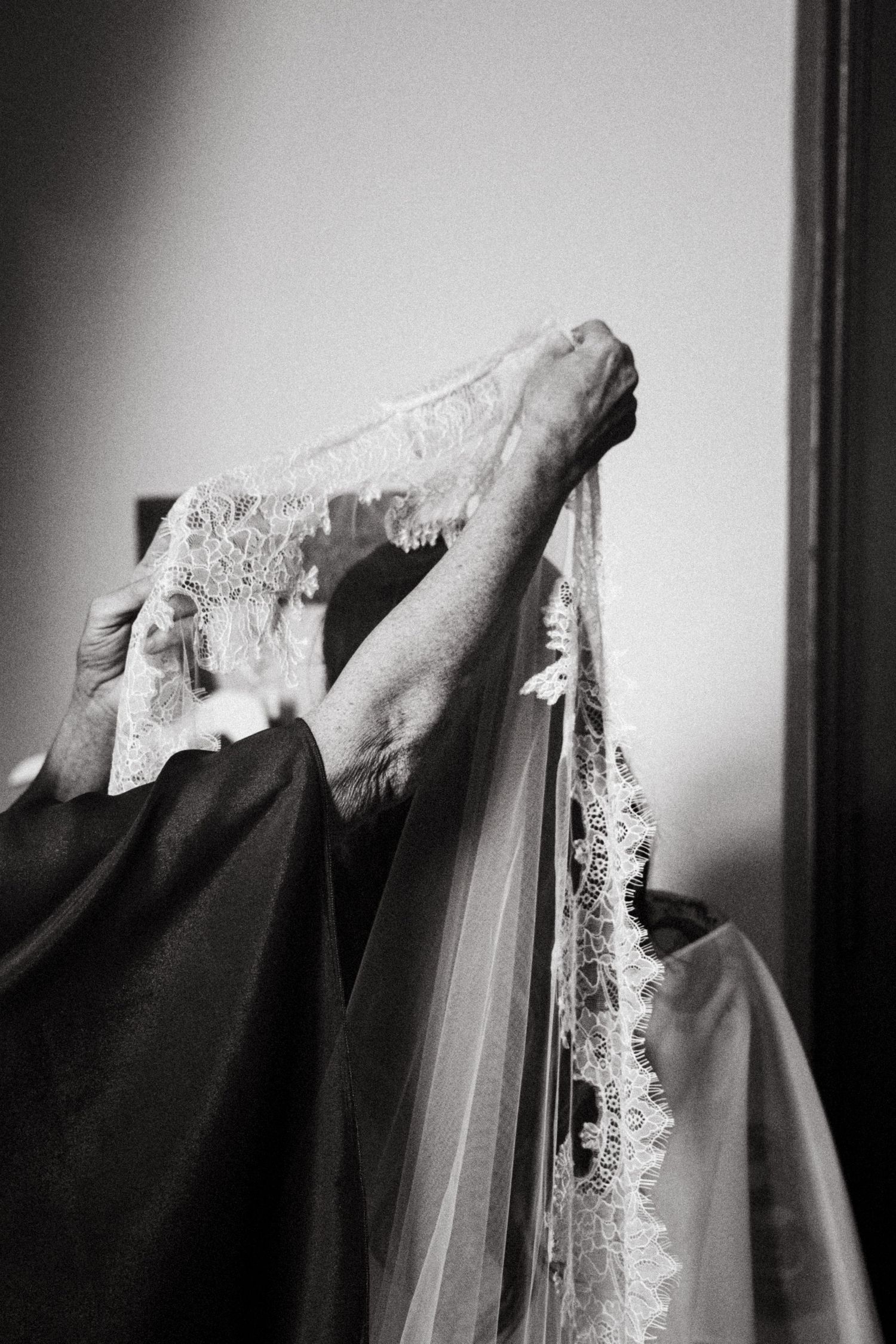 Black and white photo of hands holding a delicate lace bridal veil, wedding preparation scene.