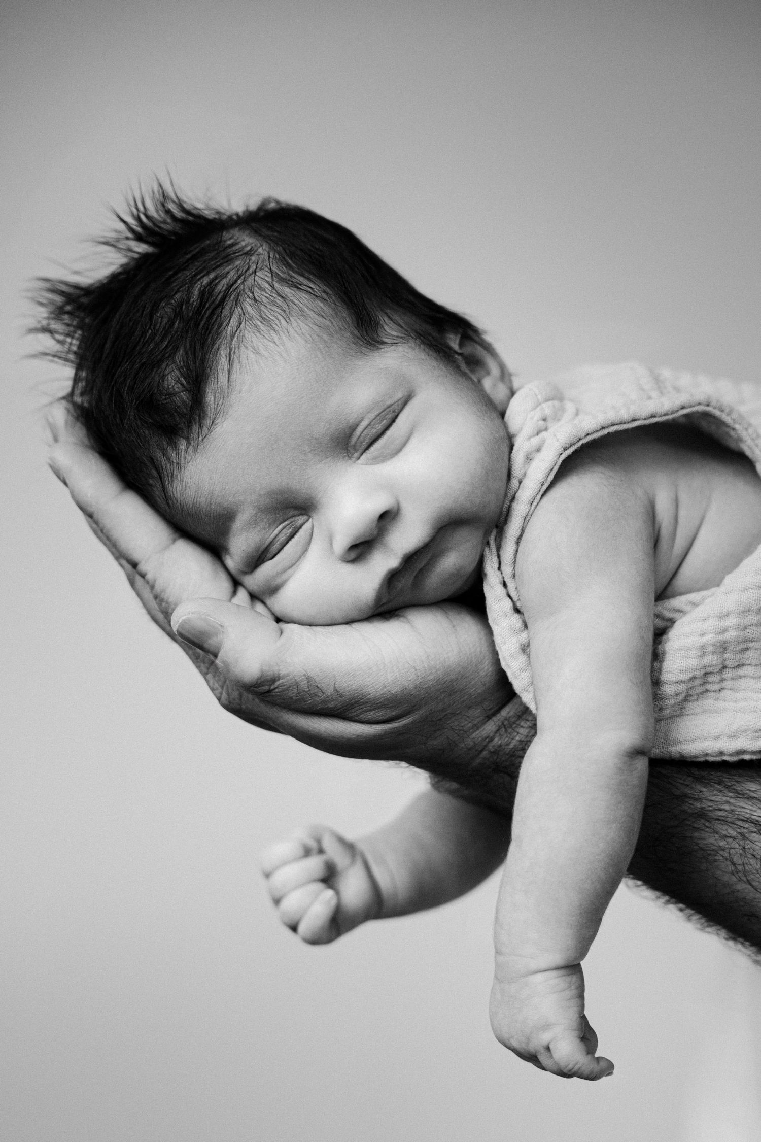 Black and white photo of a sleeping newborn baby cradled gently in an adult's hand.