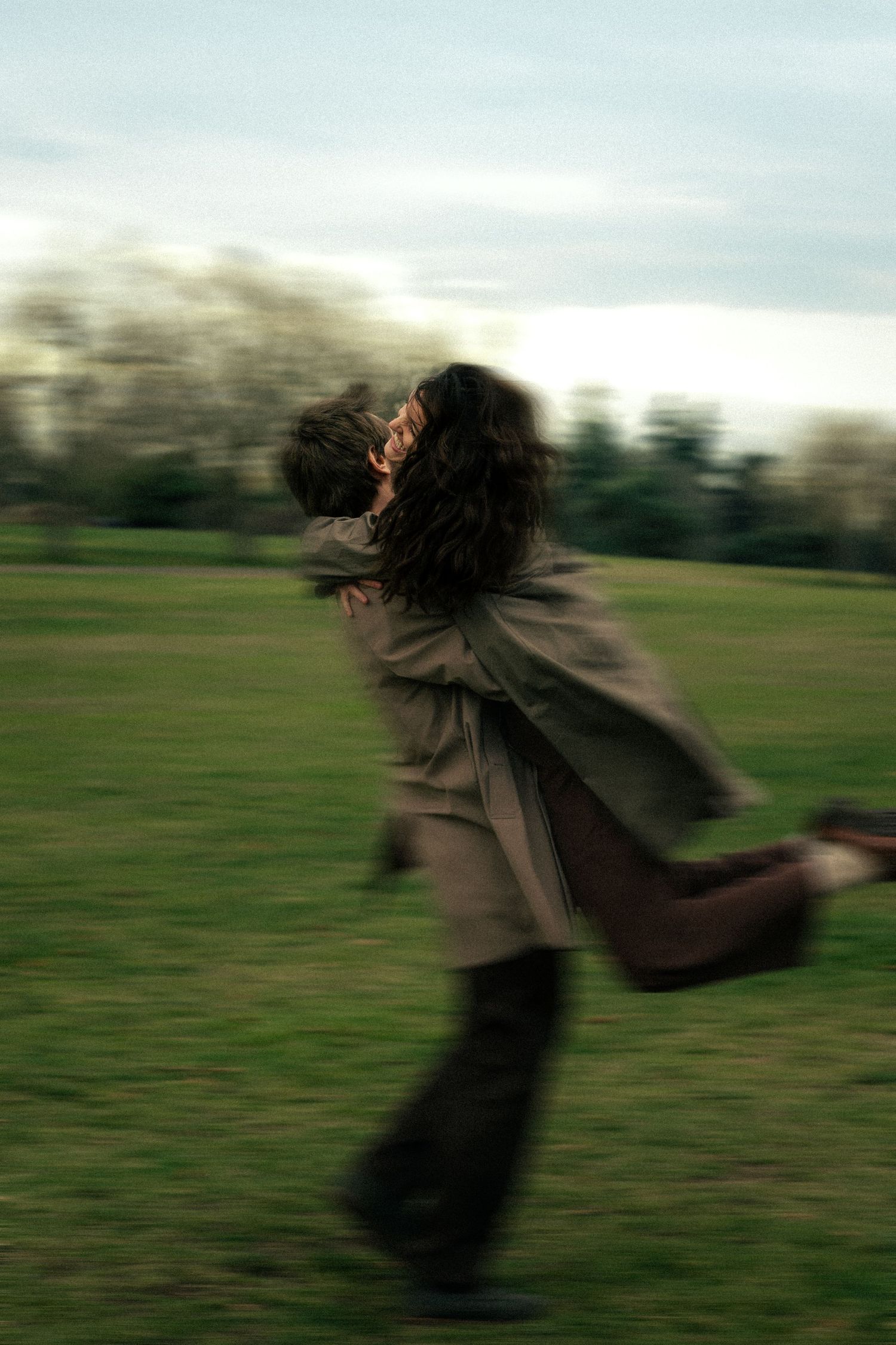 Couple embracing and spinning joyfully in a green park, motion blur capturing their playful romantic moment outdoors.