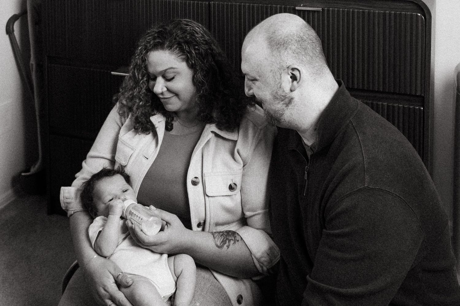 Black and white photo of parents lovingly gazing at their newborn baby during an intimate family portrait session.