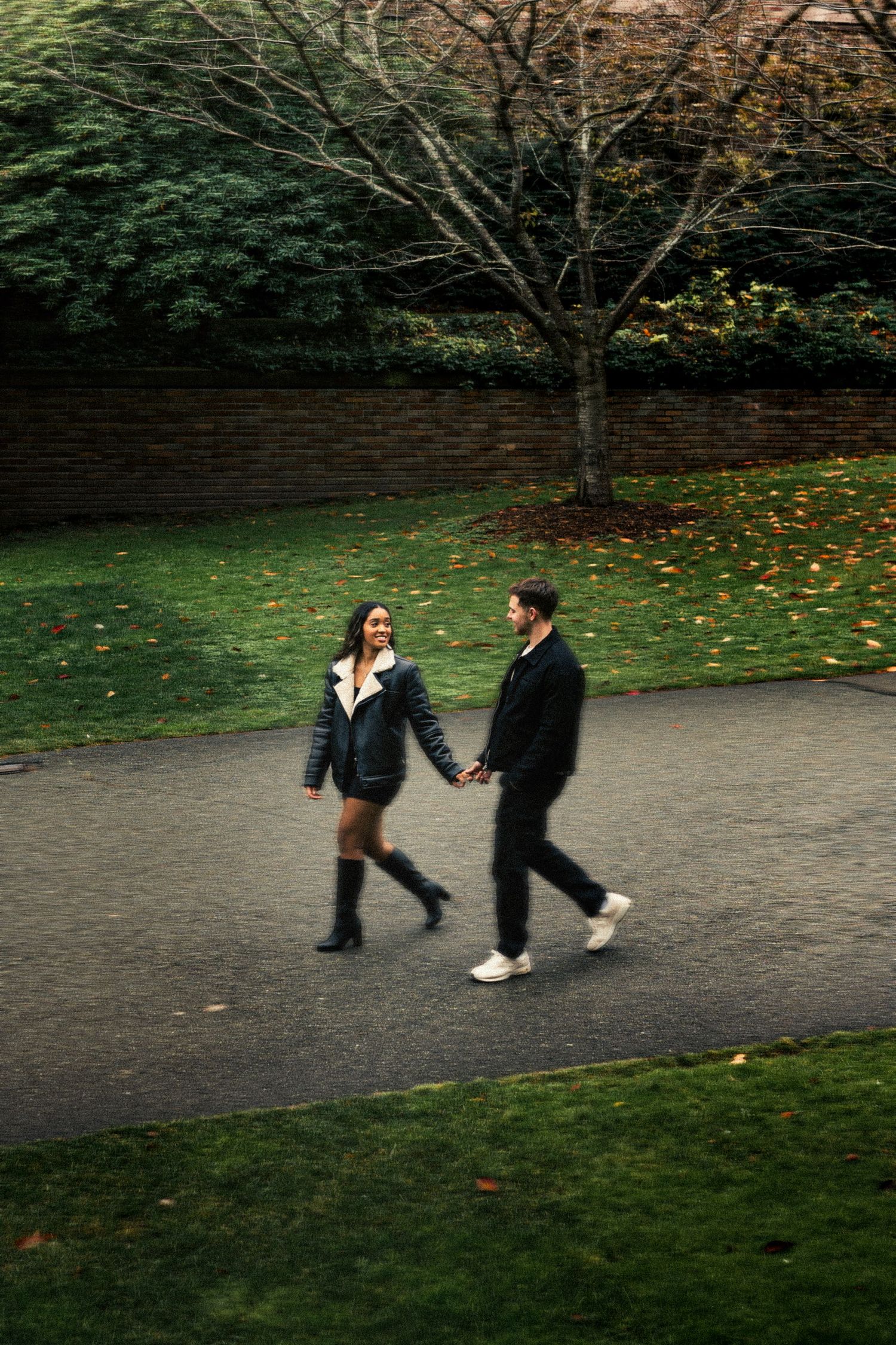 Couple holding hands and walking together on a park path surrounded by autumn foliage.