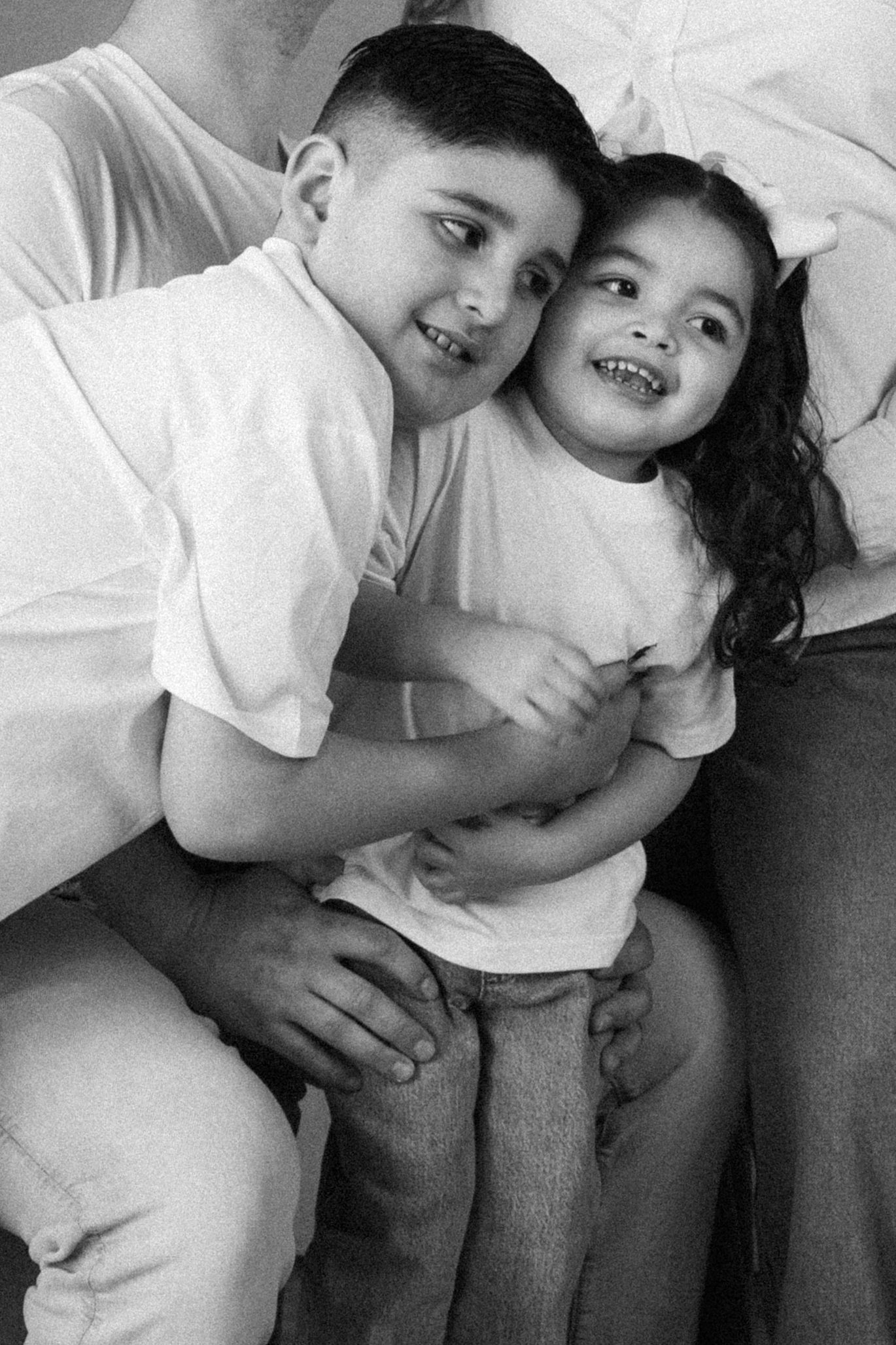 Black and white photo of a smiling boy hugging a laughing little girl, both wearing white t-shirts.