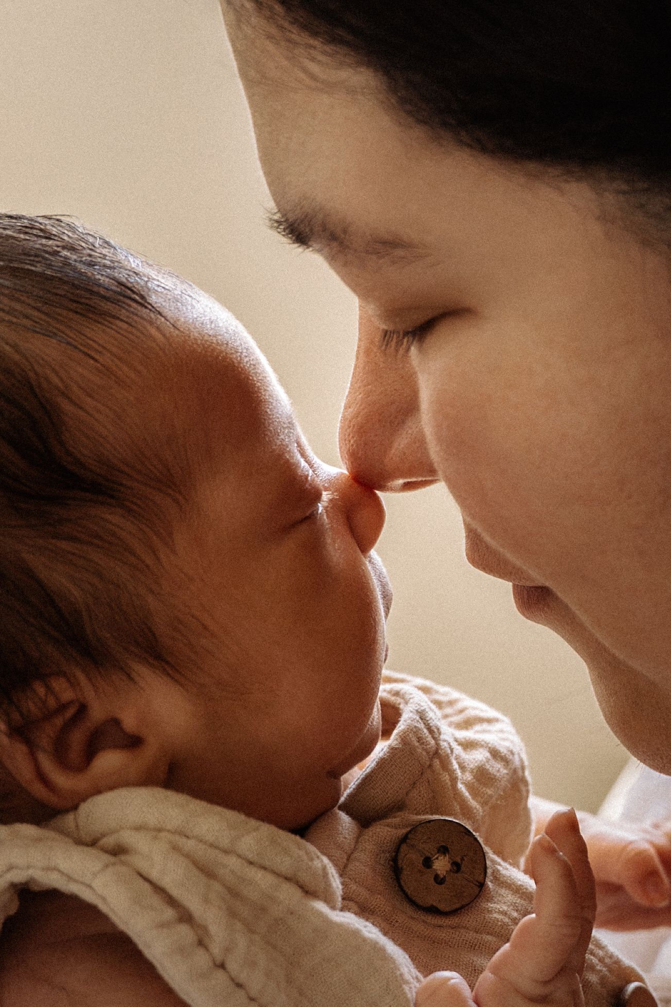 A tender moment between a mother and her newborn baby touching noses in a warm, intimate close-up portrait.