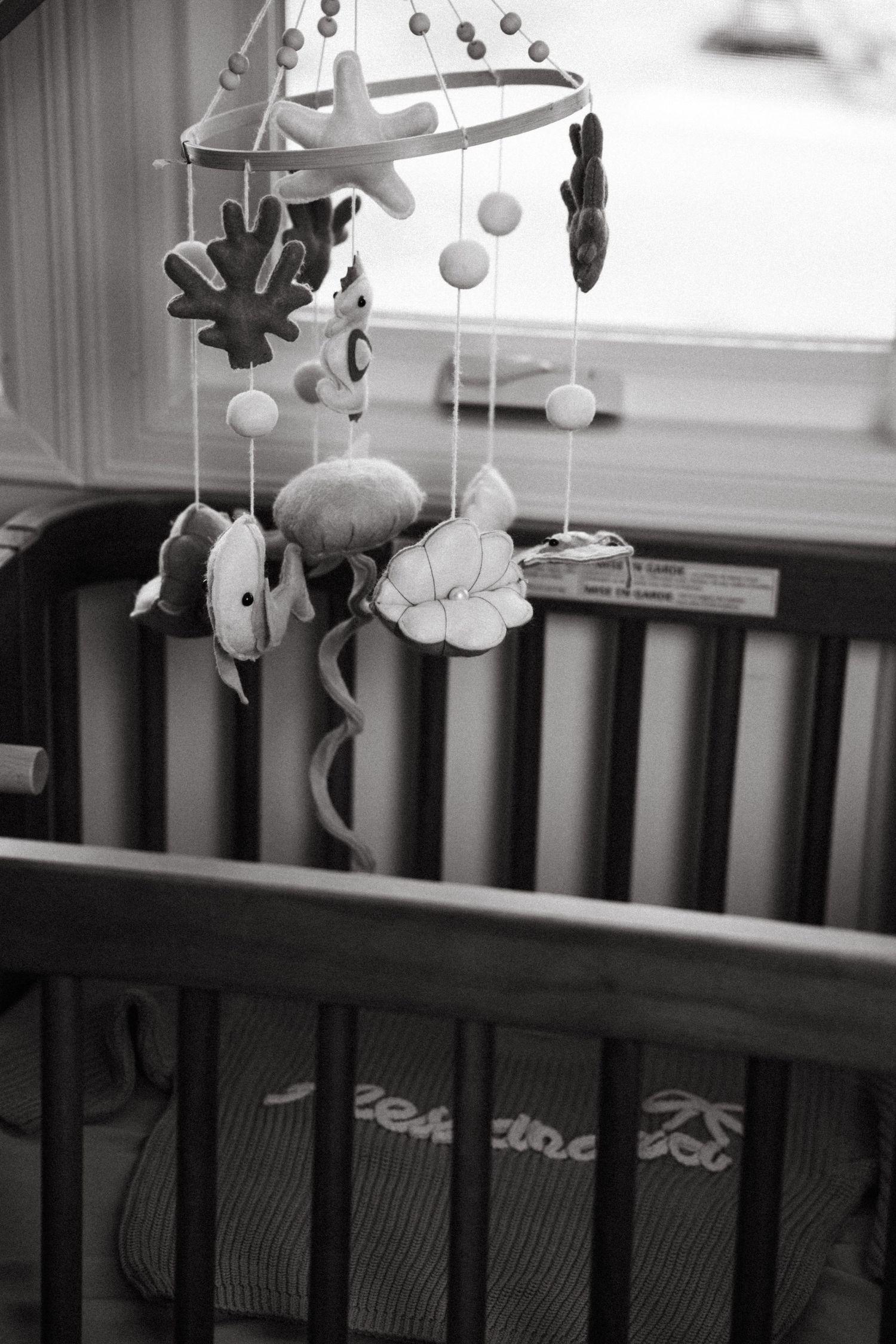 Black and white photo of a nature-themed baby mobile with plush animals hanging over a wooden crib.
