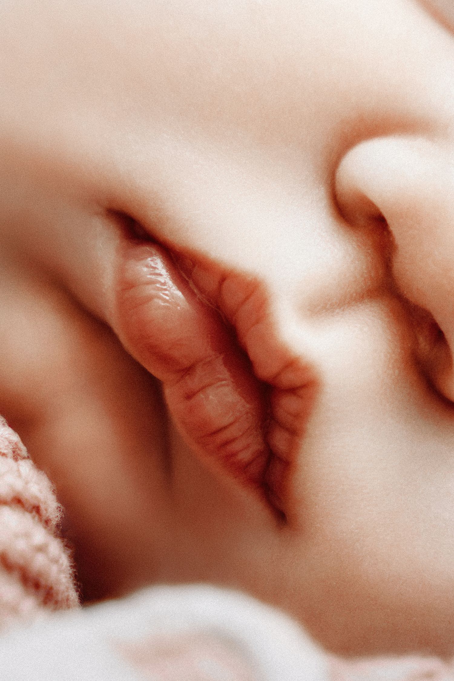 Close-up of a sleeping newborn baby's tiny hand tucked under their chin on a soft pink blanket.