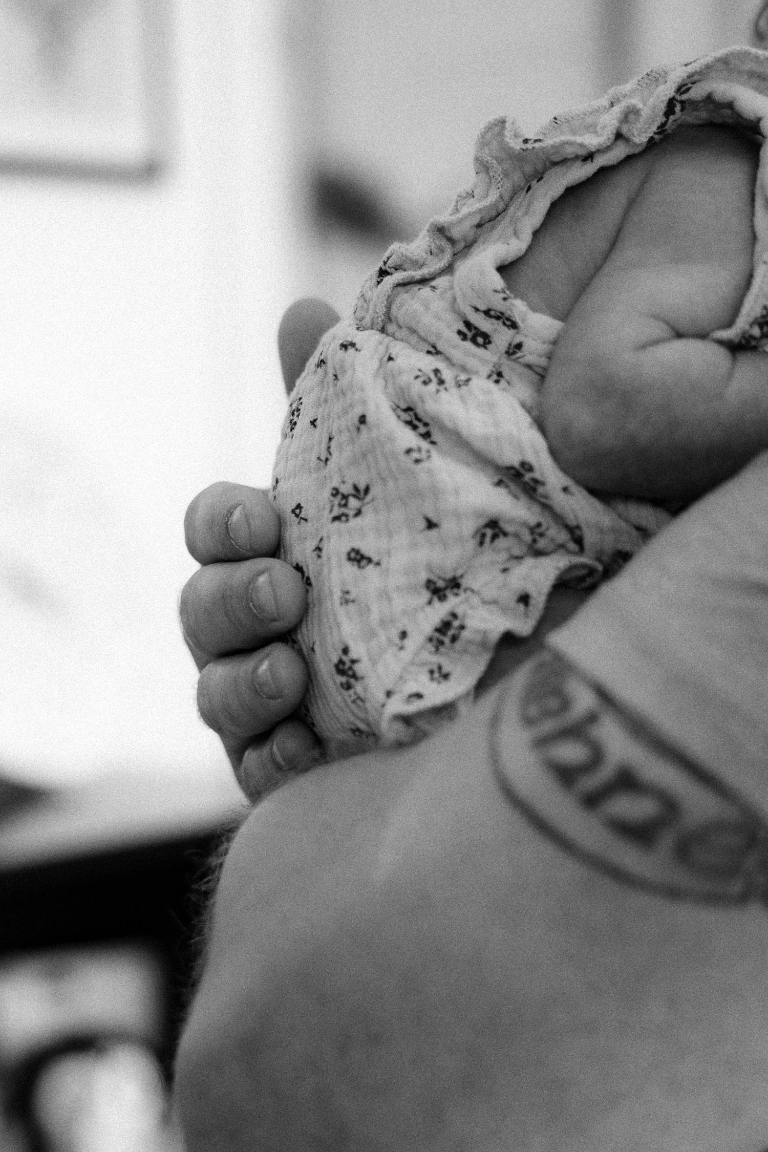 Black and white photo of a newborn baby being cradled by an adult with a tattoo on their arm.