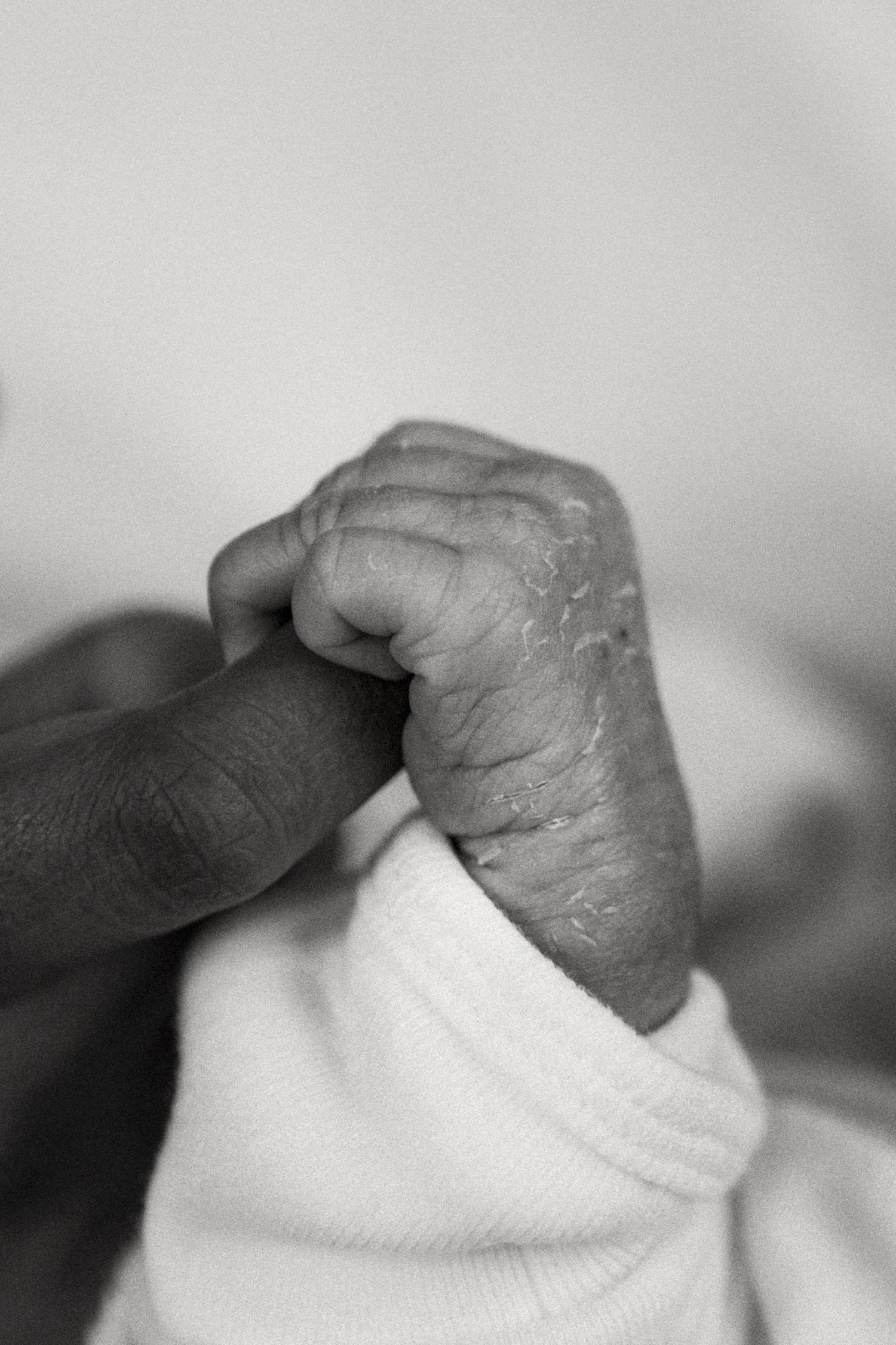Black and white close-up of a newborn baby's tiny hand grasping an adult's finger tenderly.