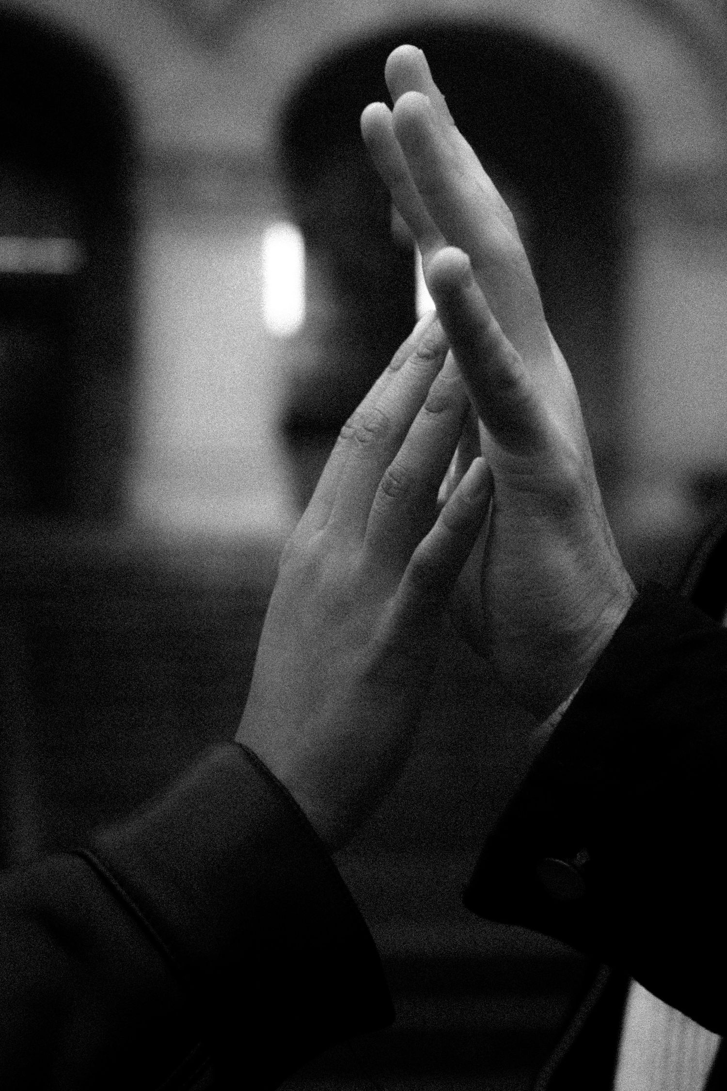 Black and white photo of two hands pressed together in prayer gesture against blurred background.