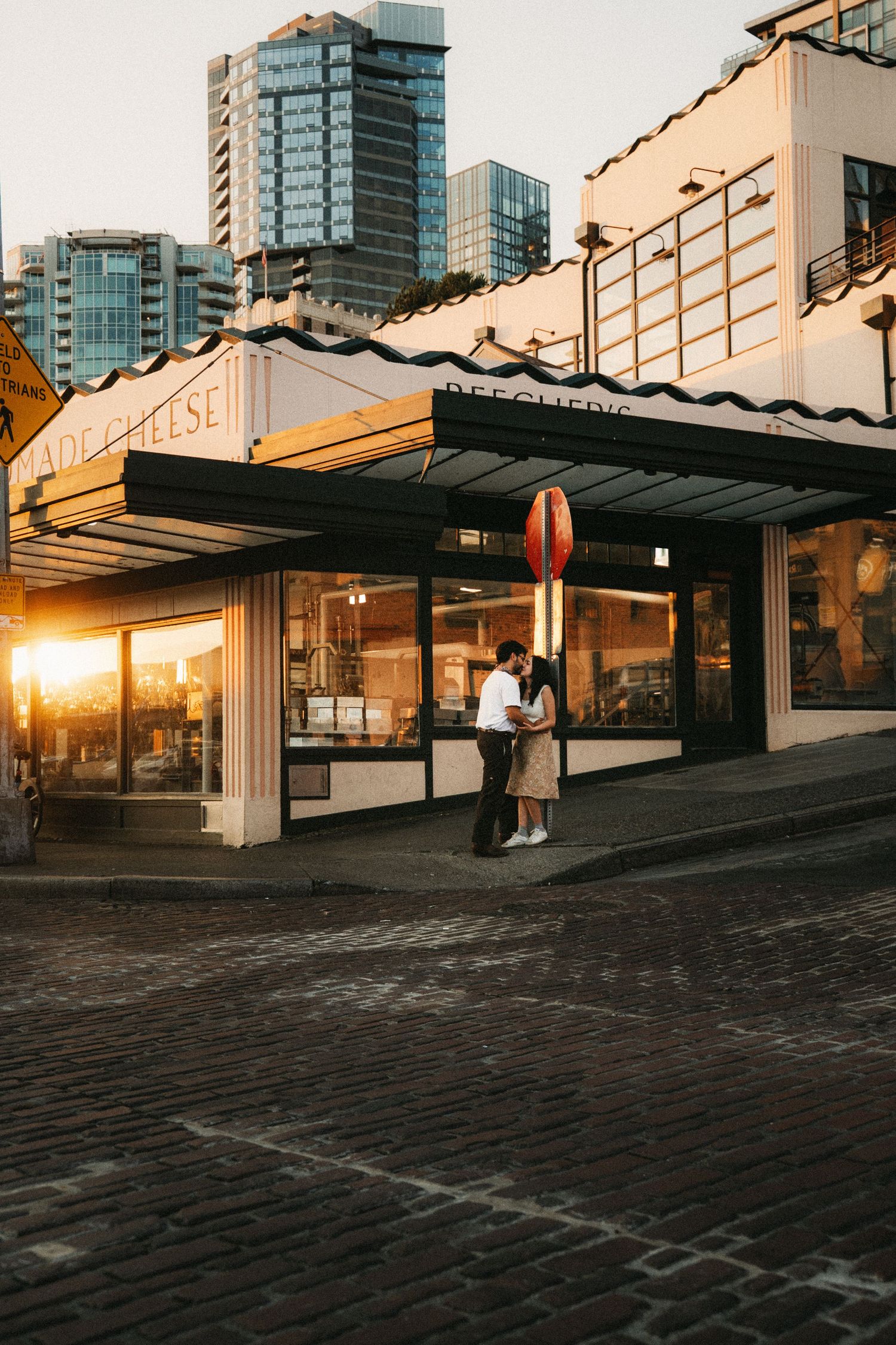 Couple embracing at golden hour outside Pike Place Market cheese shop, Seattle skyline visible in background.