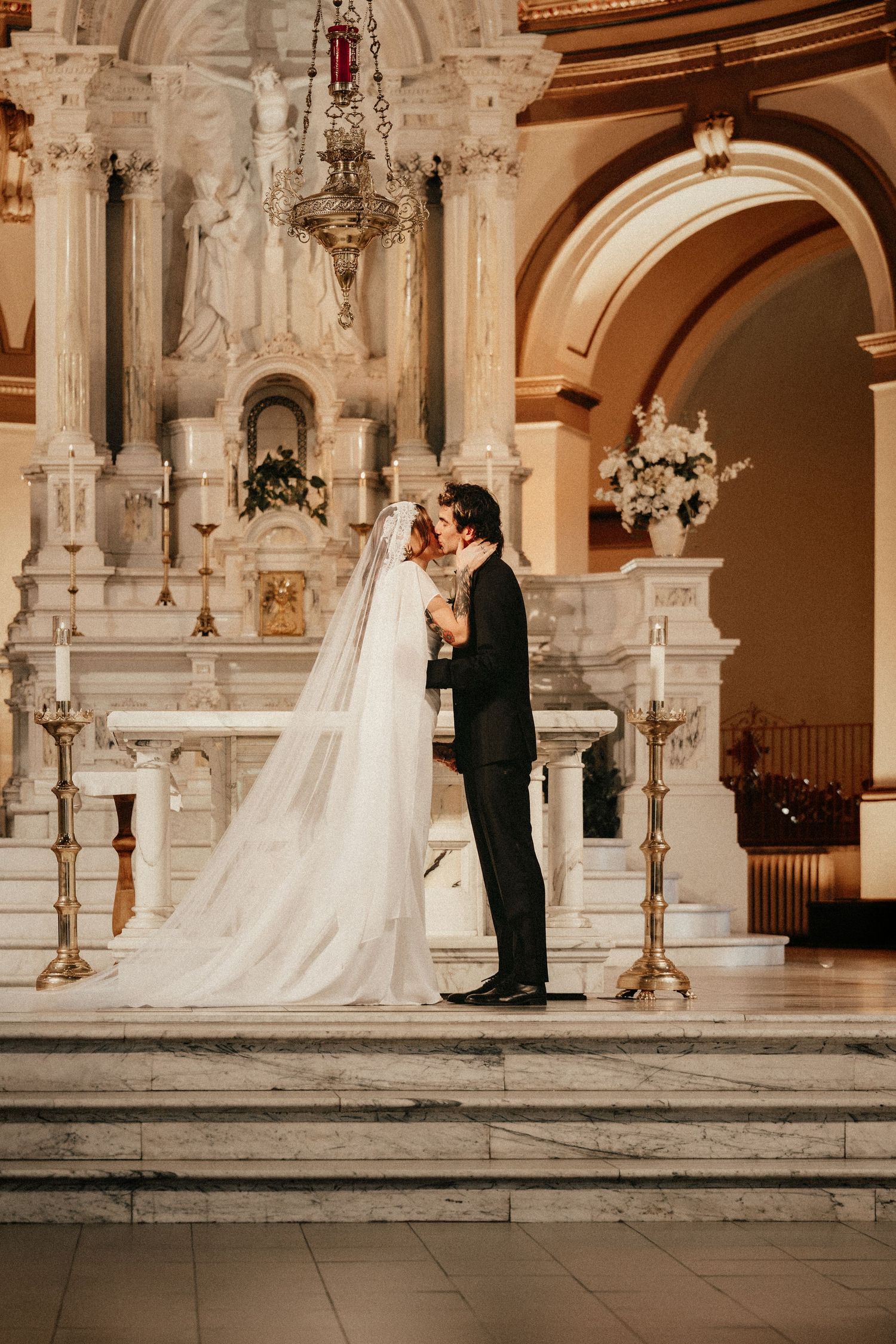 Bride and groom share a kiss at the altar of an elegant marble church during their wedding ceremony.