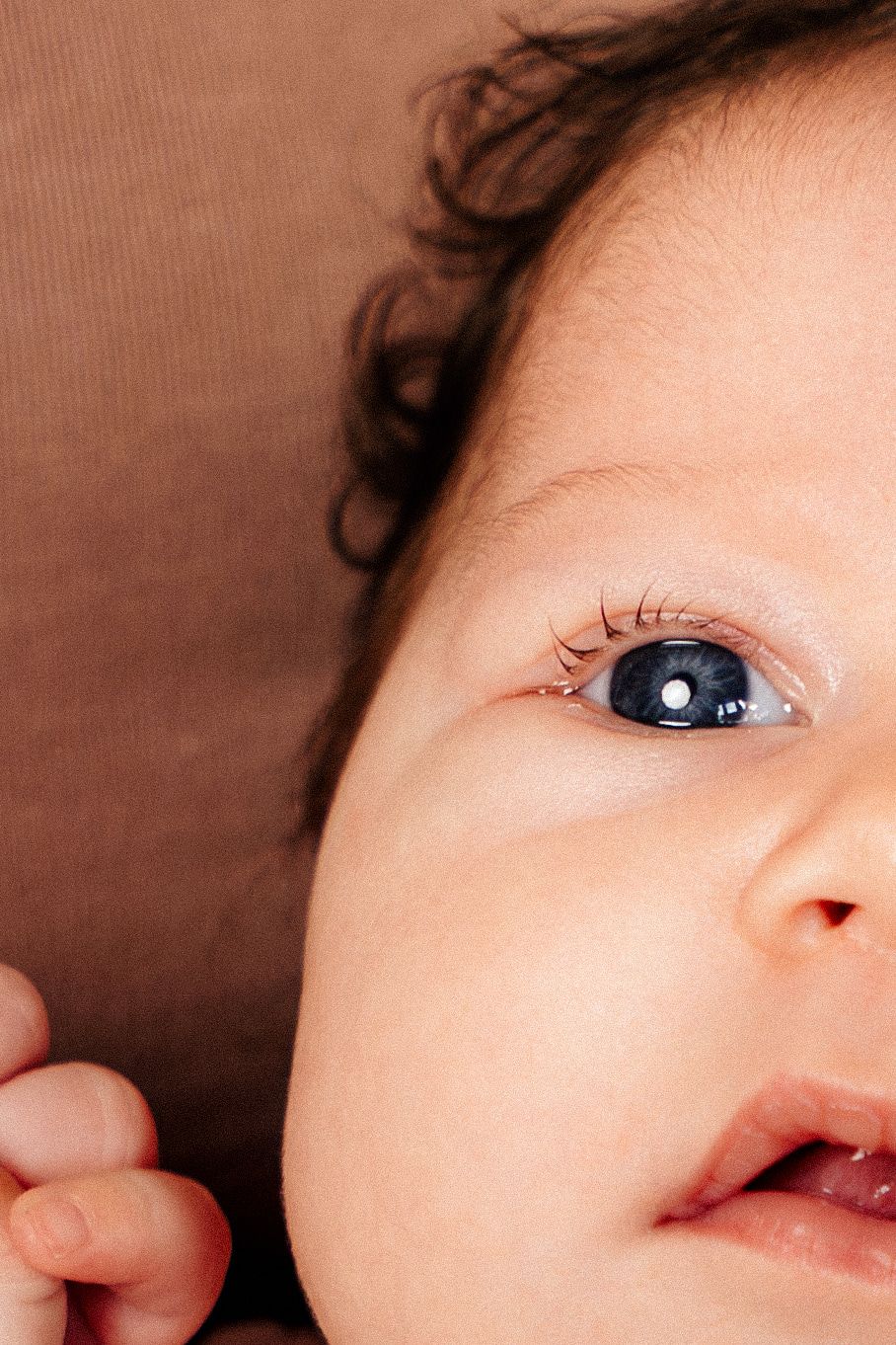 Close-up portrait of a baby with blue eyes and curly dark hair, gazing upward with a gentle expression.